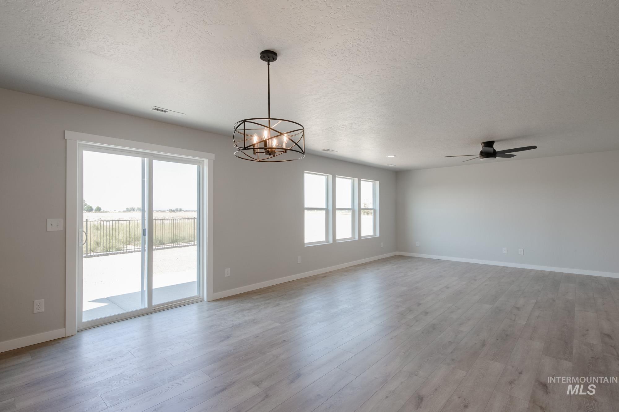 Empty room featuring a textured ceiling, a chandelier, light wood finished floors, and a ceiling fan