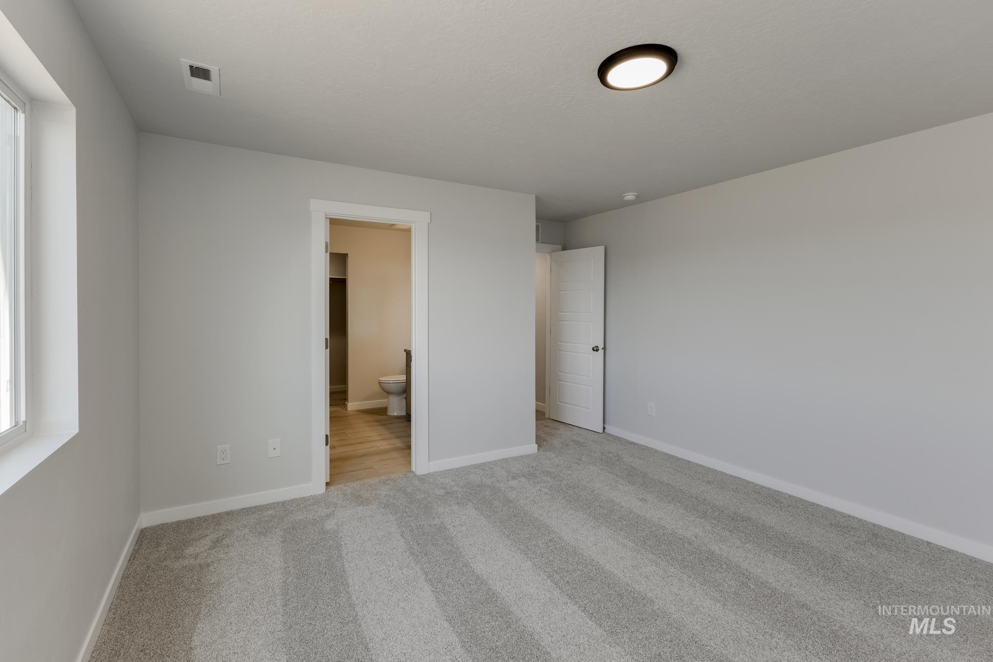 Unfurnished bedroom with light carpet and ensuite bathroom
