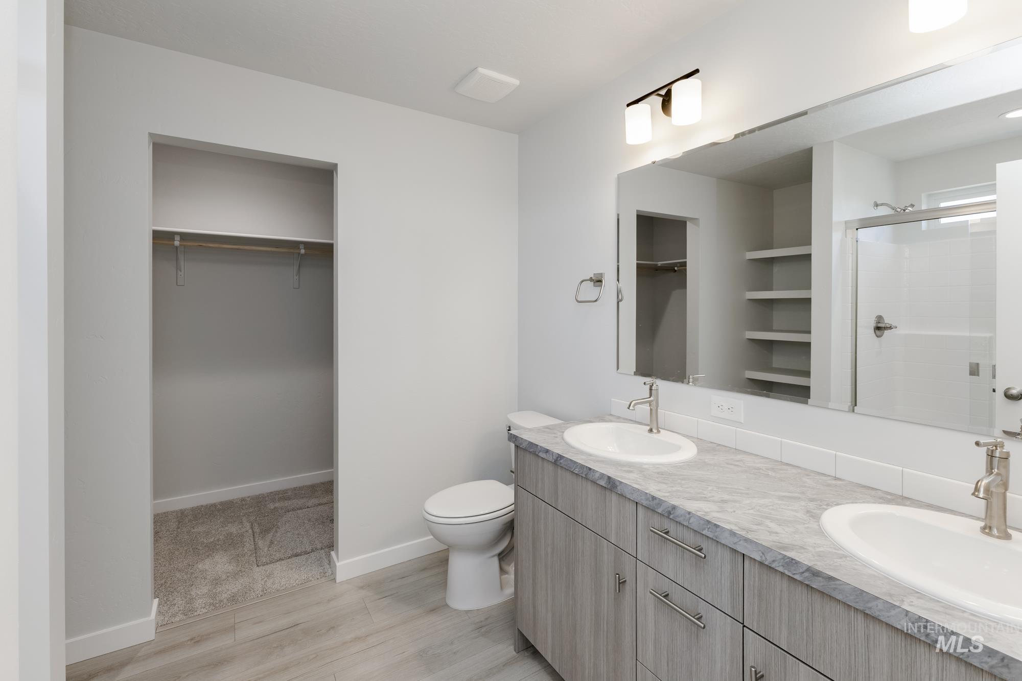 Full bathroom with a walk in closet, double vanity, wood finished floors, and a shower with shower door