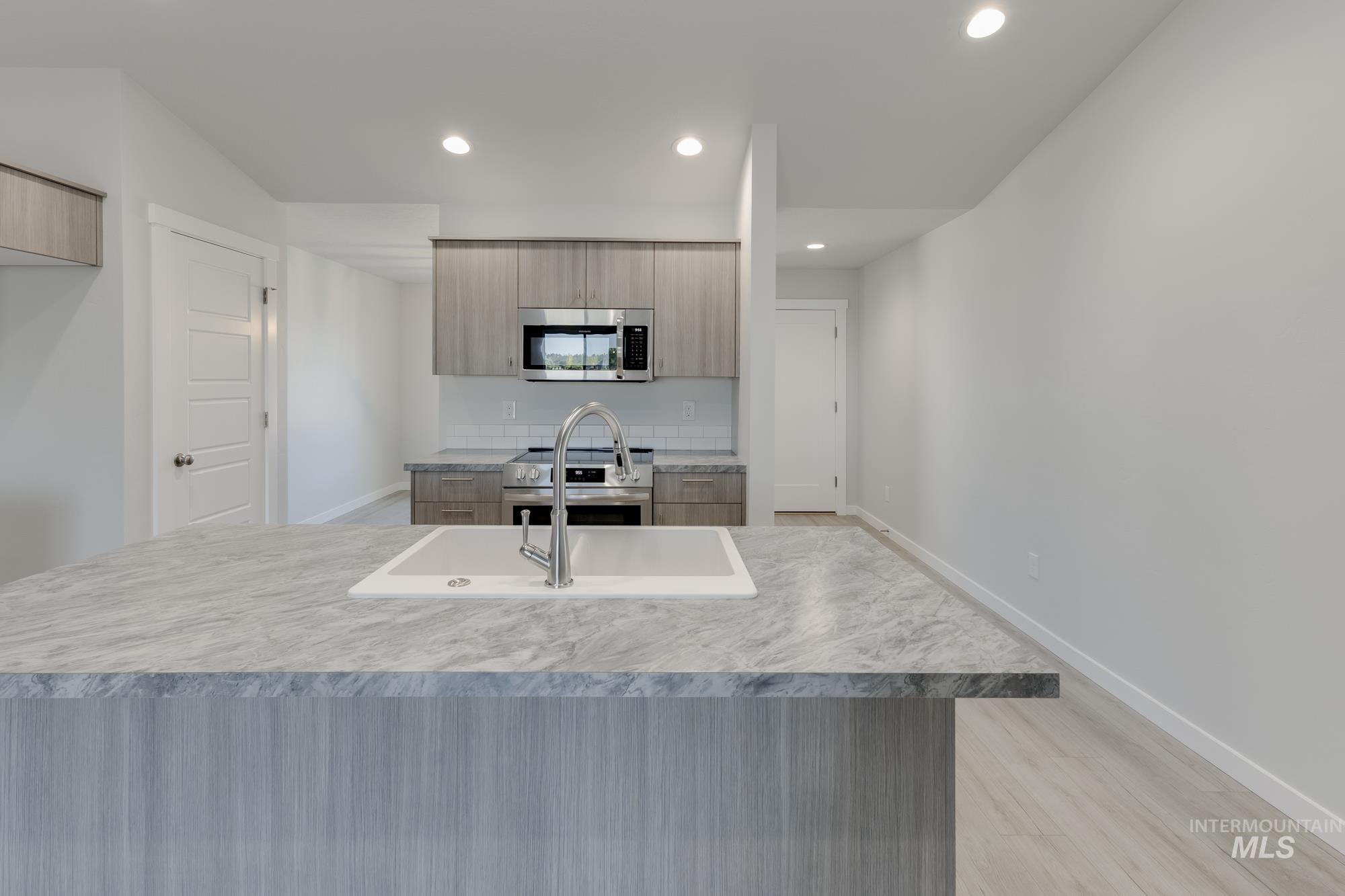 Kitchen with modern cabinets, stainless steel appliances, light wood-style flooring, recessed lighting, and light countertops
