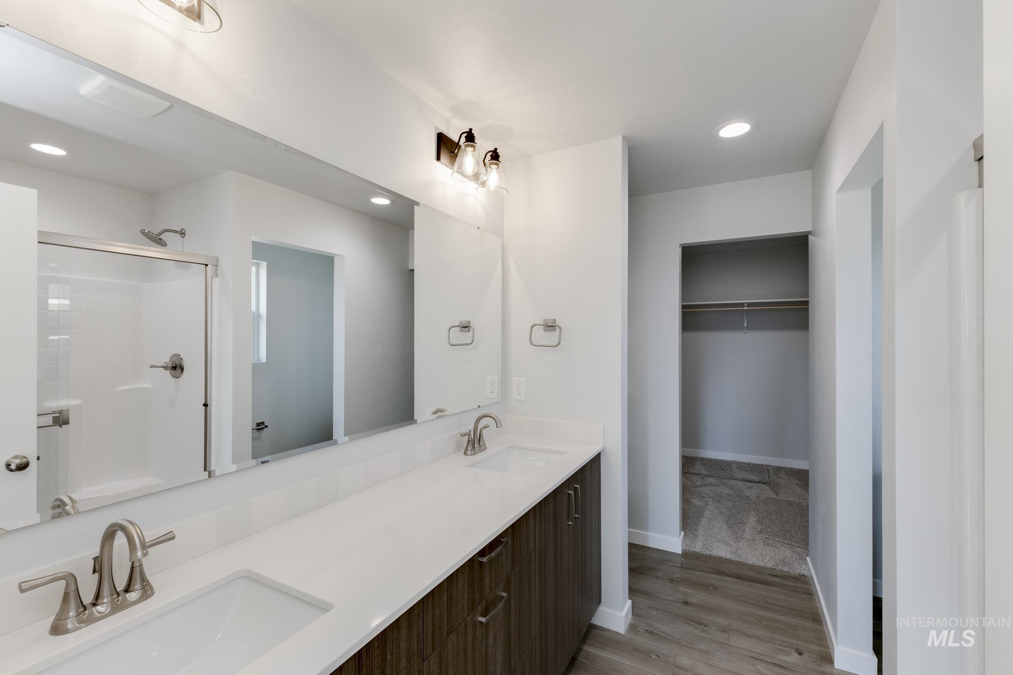 Full bath with recessed lighting, a spacious closet, double vanity, light wood finished floors, and a stall shower