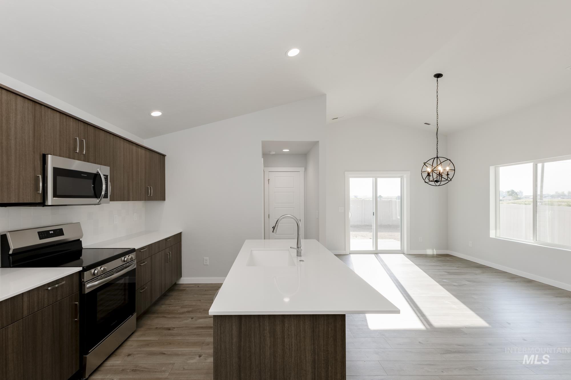 Kitchen featuring appliances with stainless steel finishes, dark brown cabinets, light wood-type flooring, an island with sink, and lofted ceiling