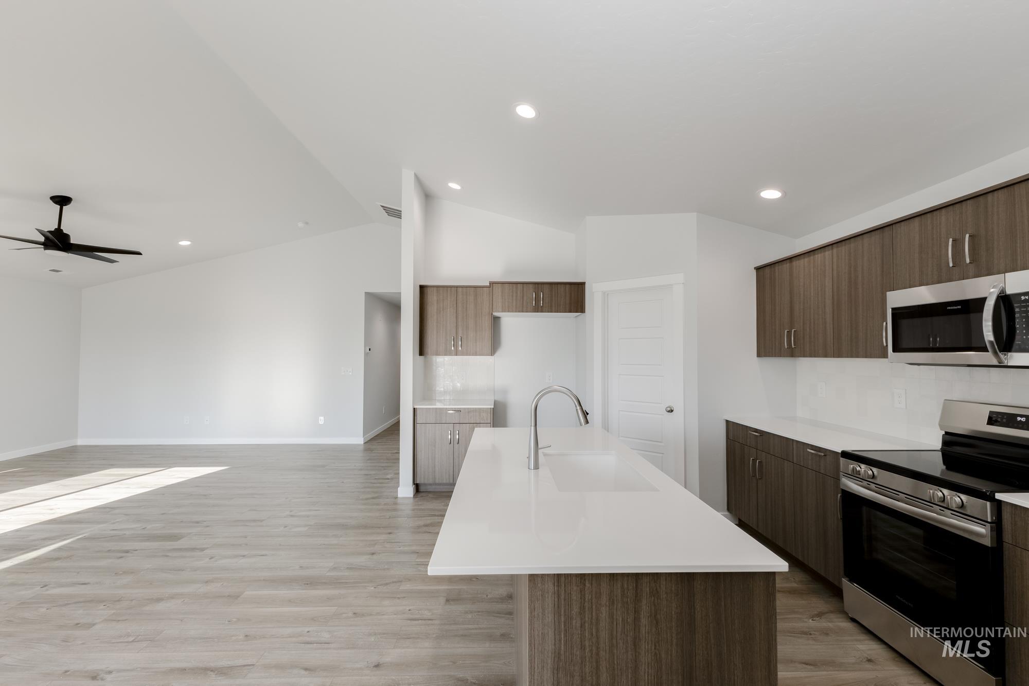 Kitchen with stainless steel appliances, modern cabinets, vaulted ceiling, an island with sink, and light wood-type flooring