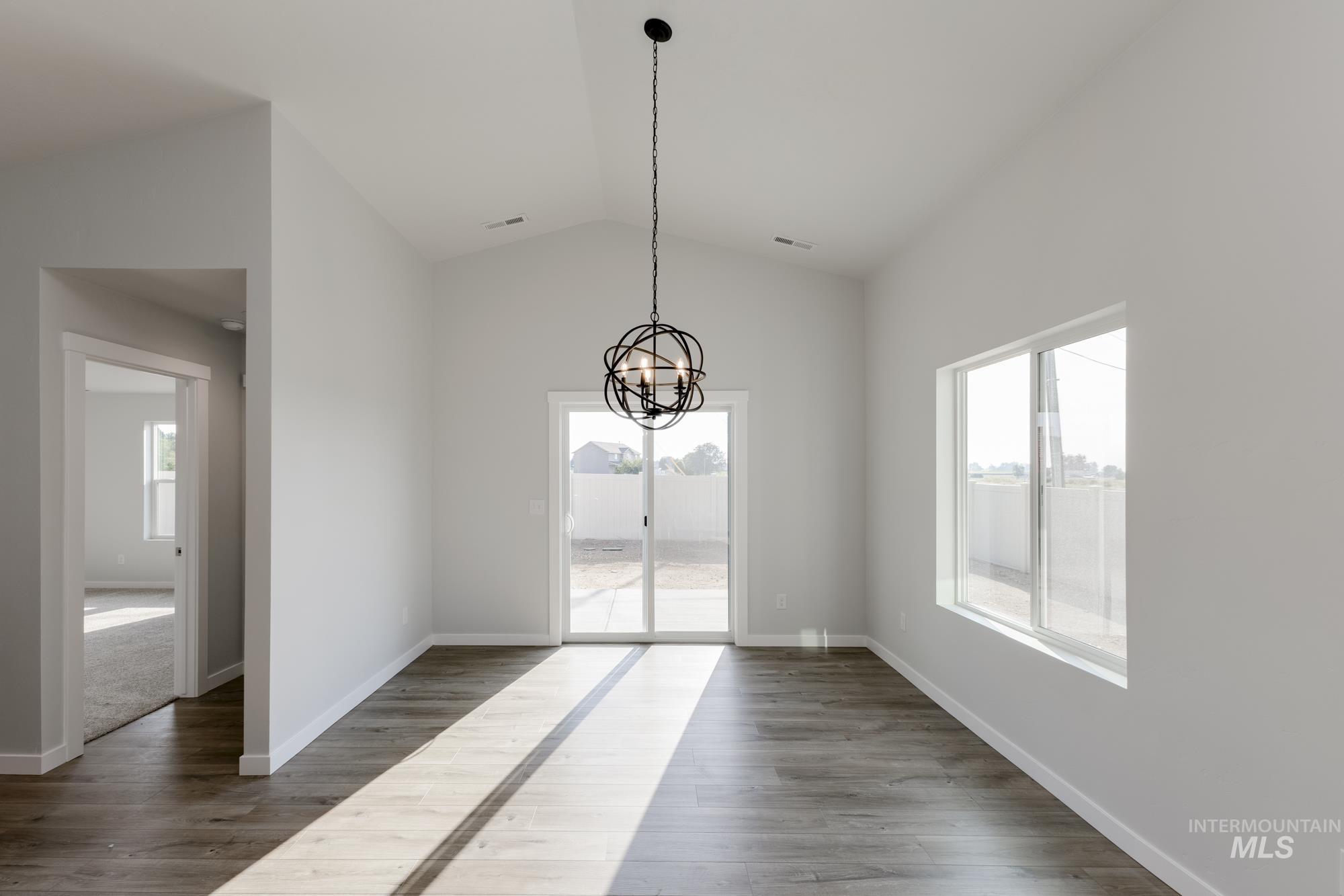 Unfurnished dining area featuring dark wood finished floors, a chandelier, and vaulted ceiling
