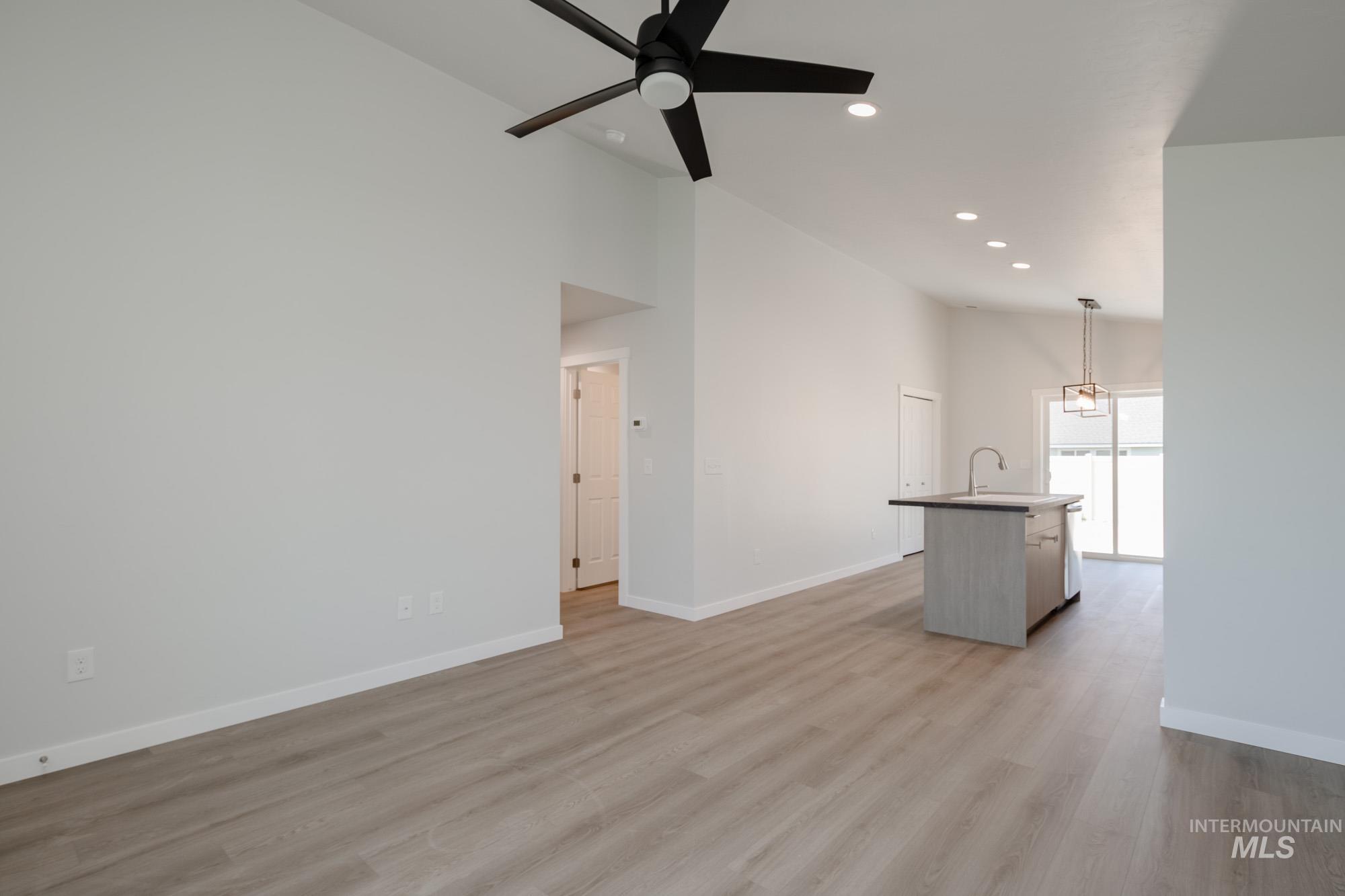 Unfurnished living room featuring light wood-type flooring, recessed lighting, ceiling fan, and a high ceiling