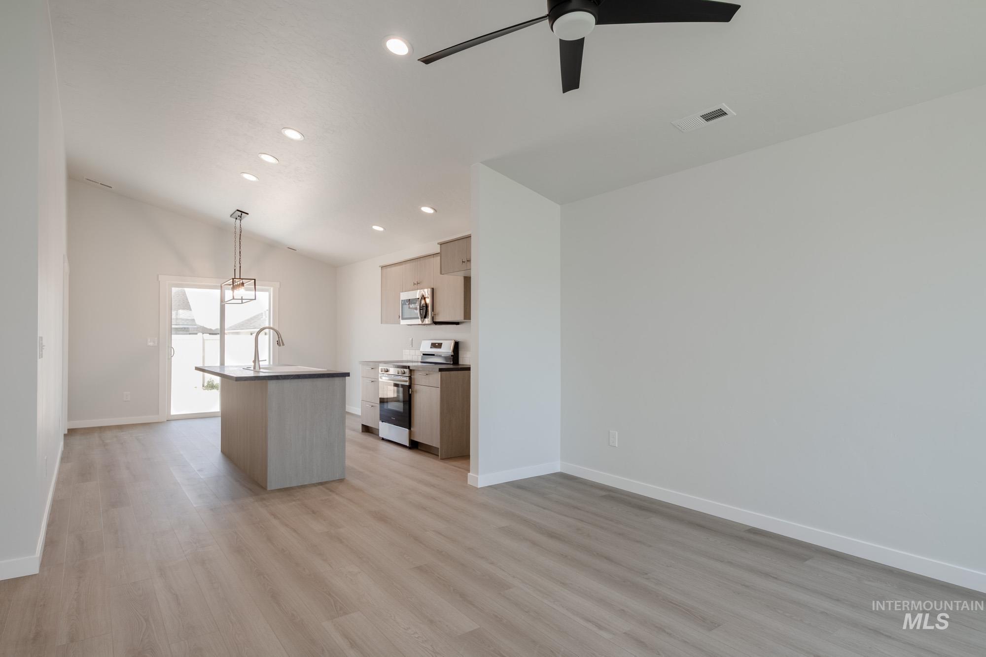 Kitchen featuring vaulted ceiling, light wood finished floors, stainless steel appliances, recessed lighting, and an island with sink