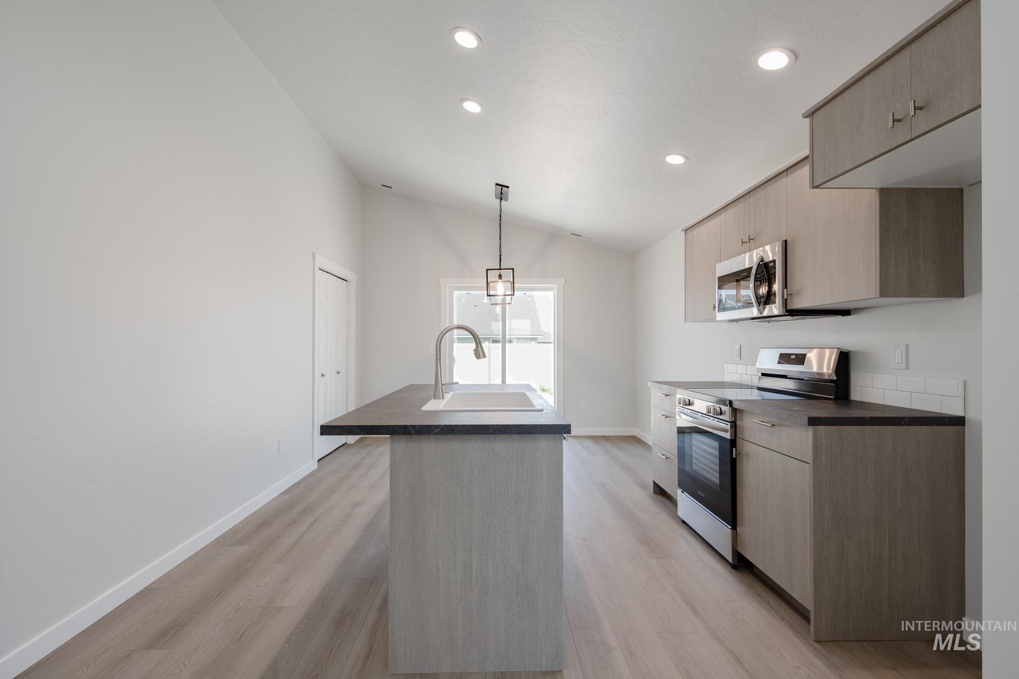Kitchen with modern cabinets, appliances with stainless steel finishes, a kitchen island with sink, dark countertops, and recessed lighting