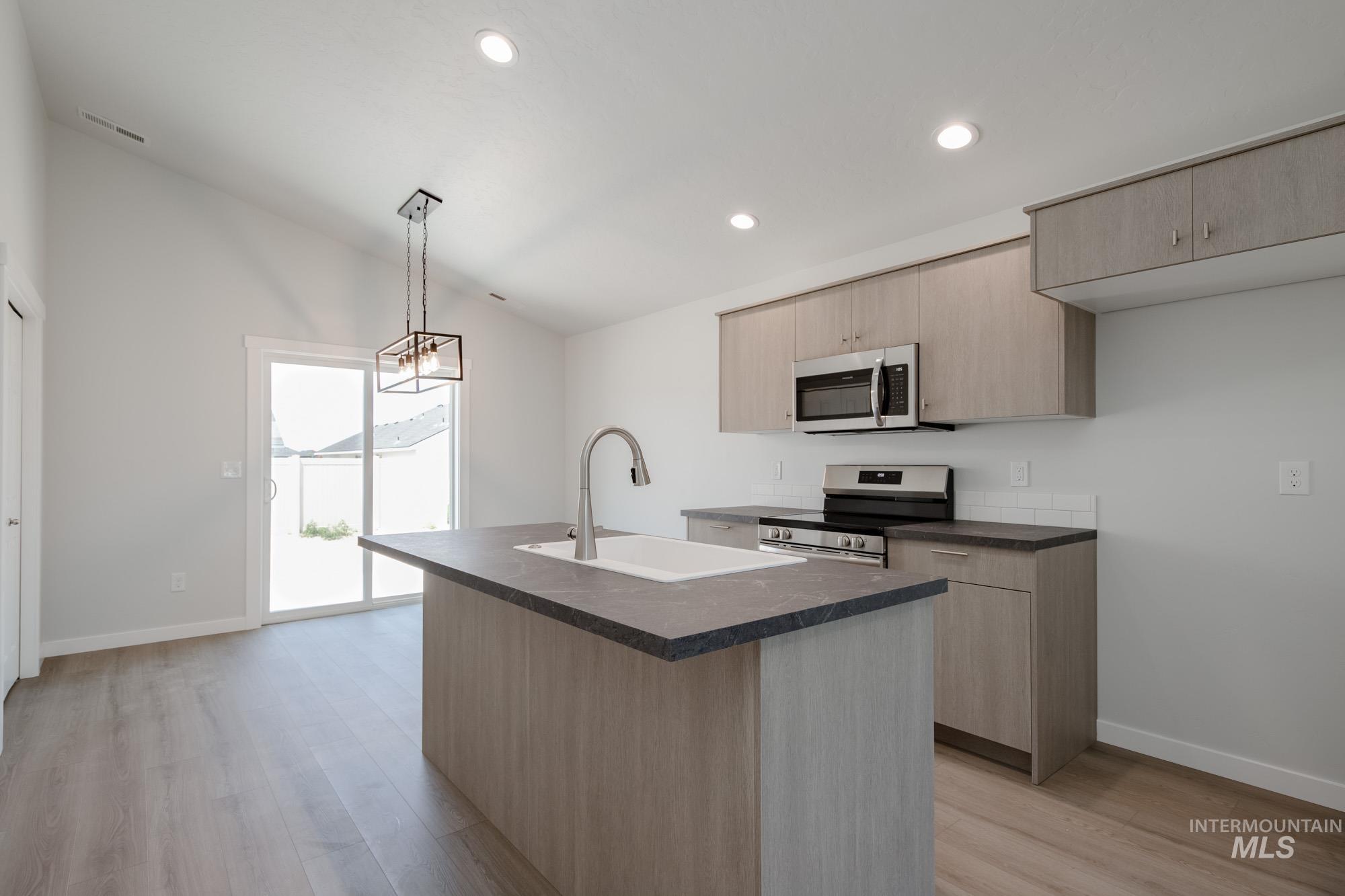 Kitchen with vaulted ceiling, dark countertops, appliances with stainless steel finishes, light brown cabinetry, and light wood finished floors
