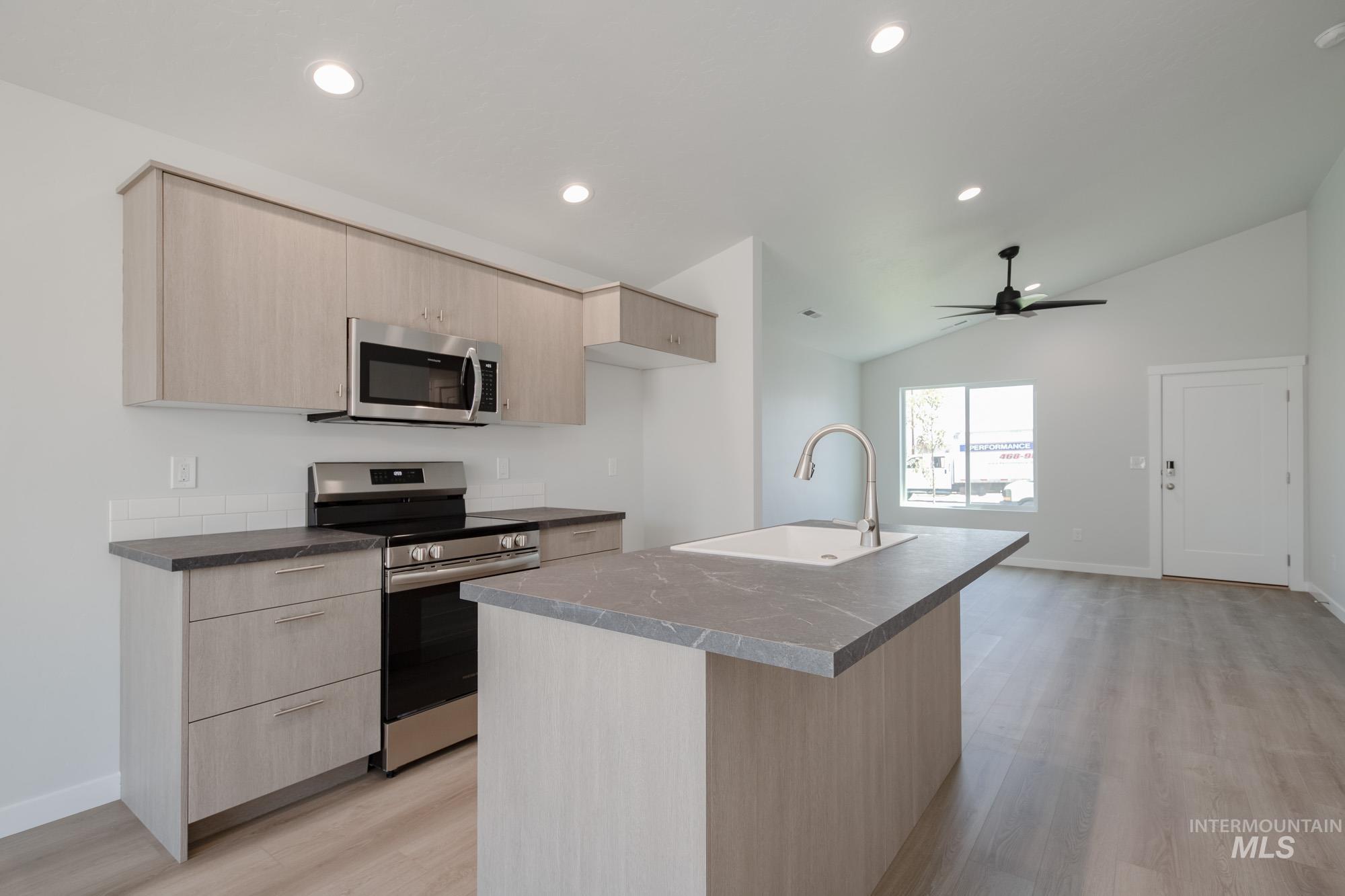 Kitchen featuring light brown cabinets, modern cabinets, stainless steel appliances, light wood-type flooring, and lofted ceiling