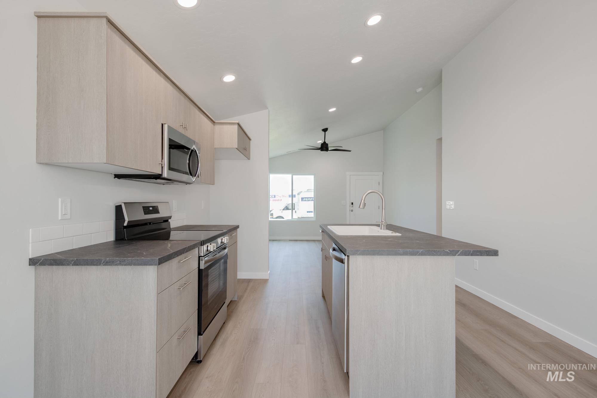 Kitchen featuring light brown cabinetry, stainless steel appliances, modern cabinets, dark countertops, and light wood-style flooring