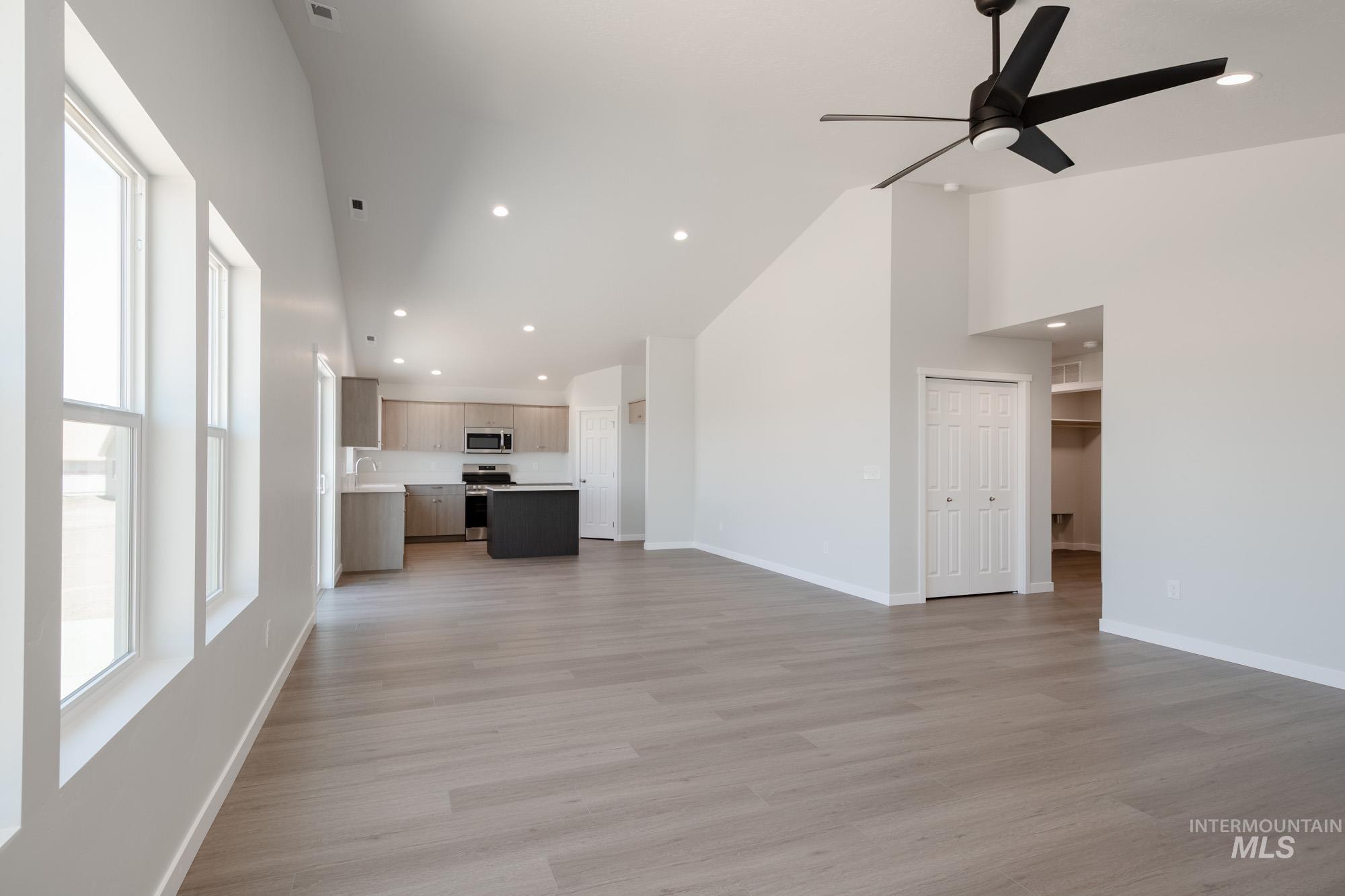 Unfurnished living room featuring ceiling fan, light wood-style flooring, high vaulted ceiling, and recessed lighting