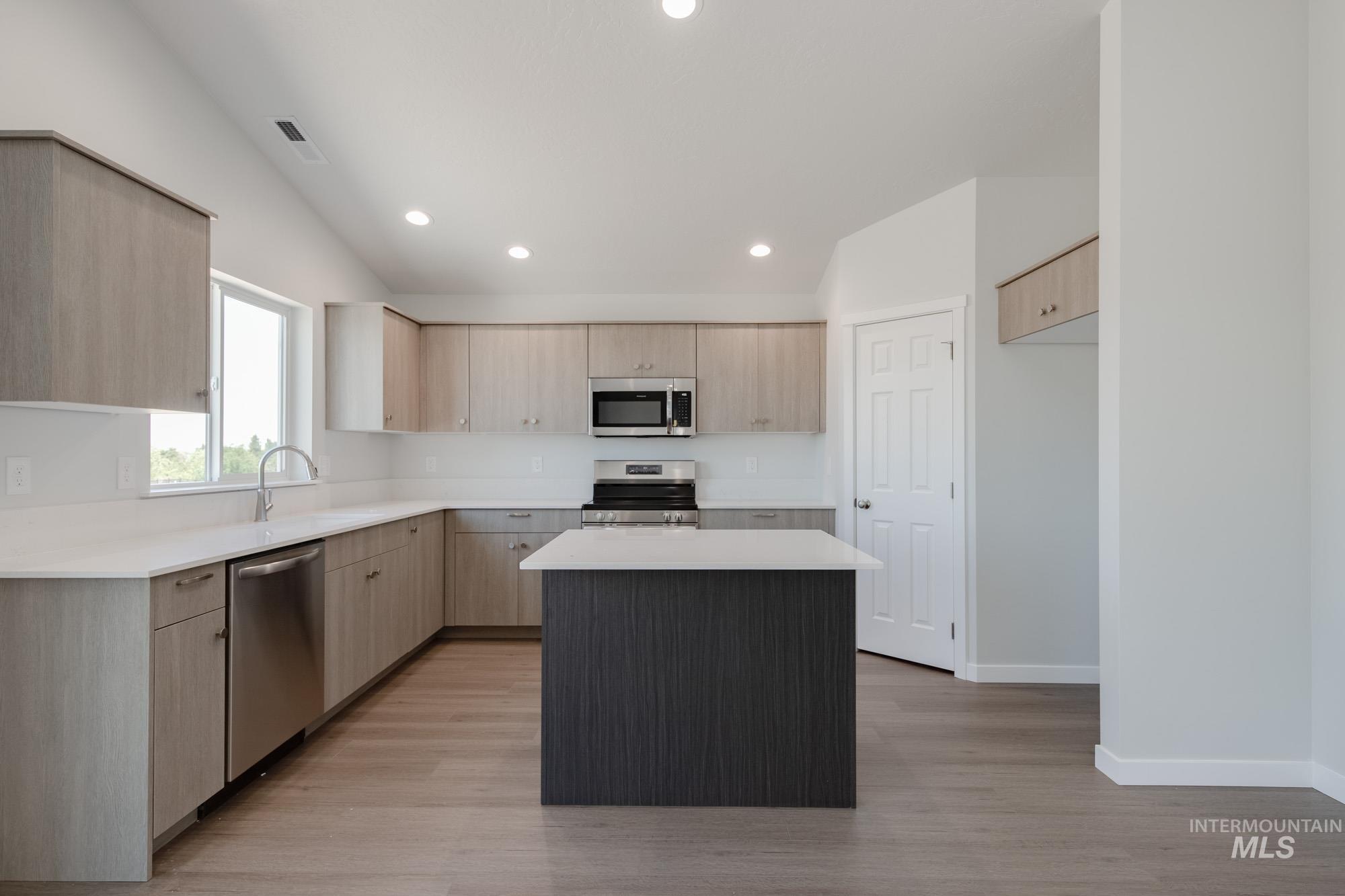 Kitchen with light brown cabinetry, stainless steel appliances, light countertops, a kitchen island, and light wood-style flooring