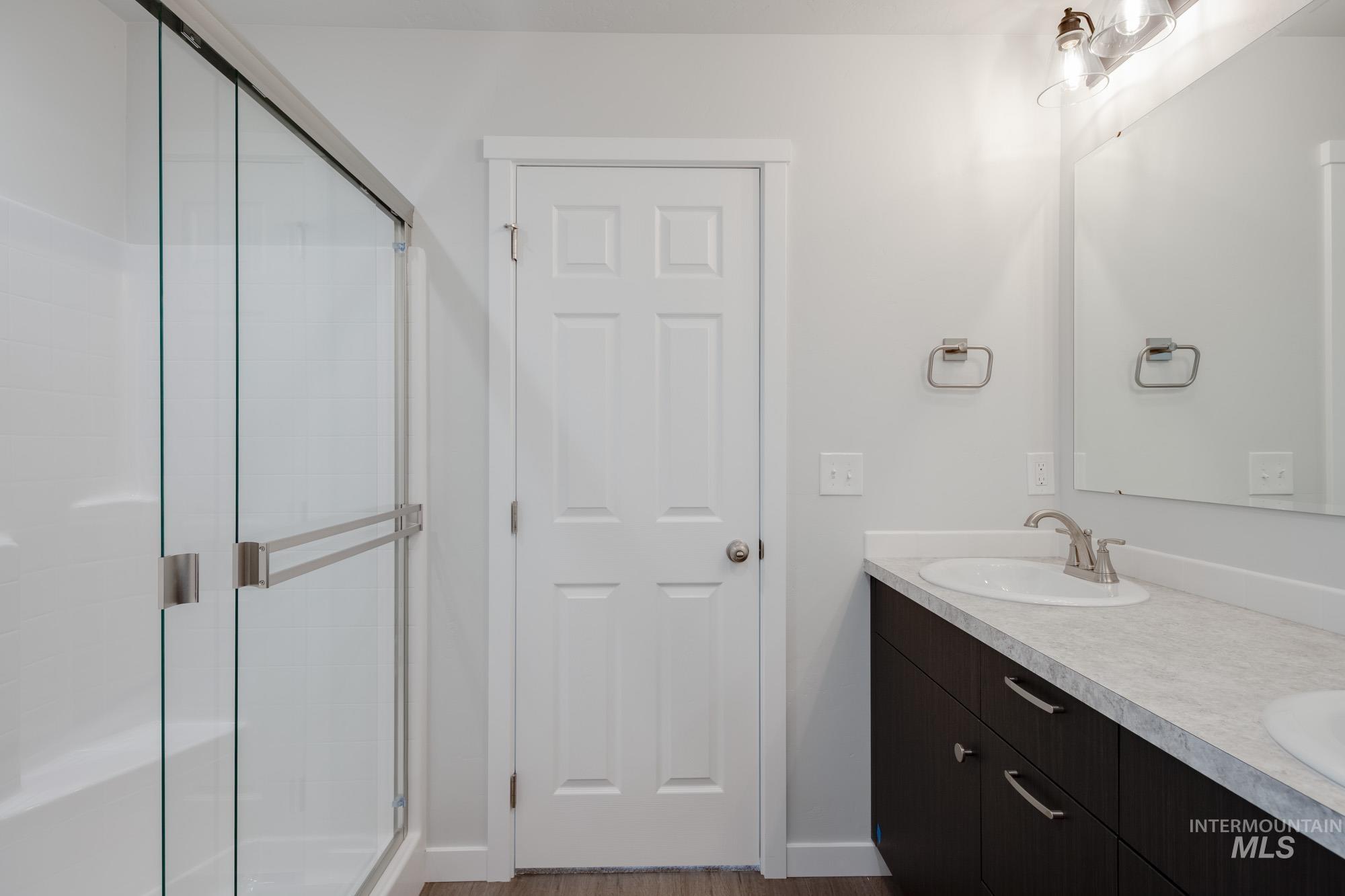 Full bathroom with a shower stall, double vanity, and wood finished floors