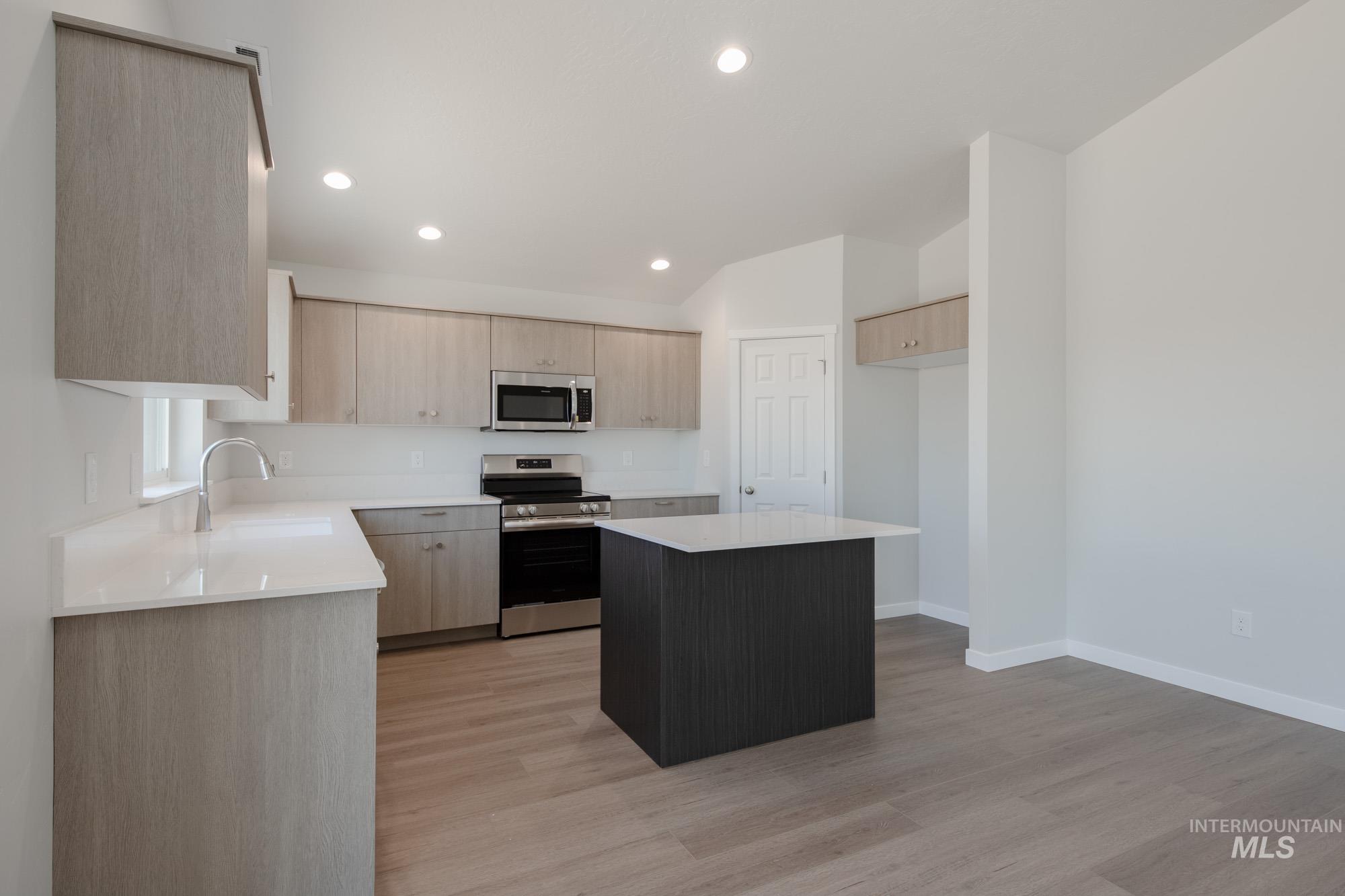 Kitchen with light brown cabinetry, stainless steel appliances, a center island, light wood-type flooring, and recessed lighting