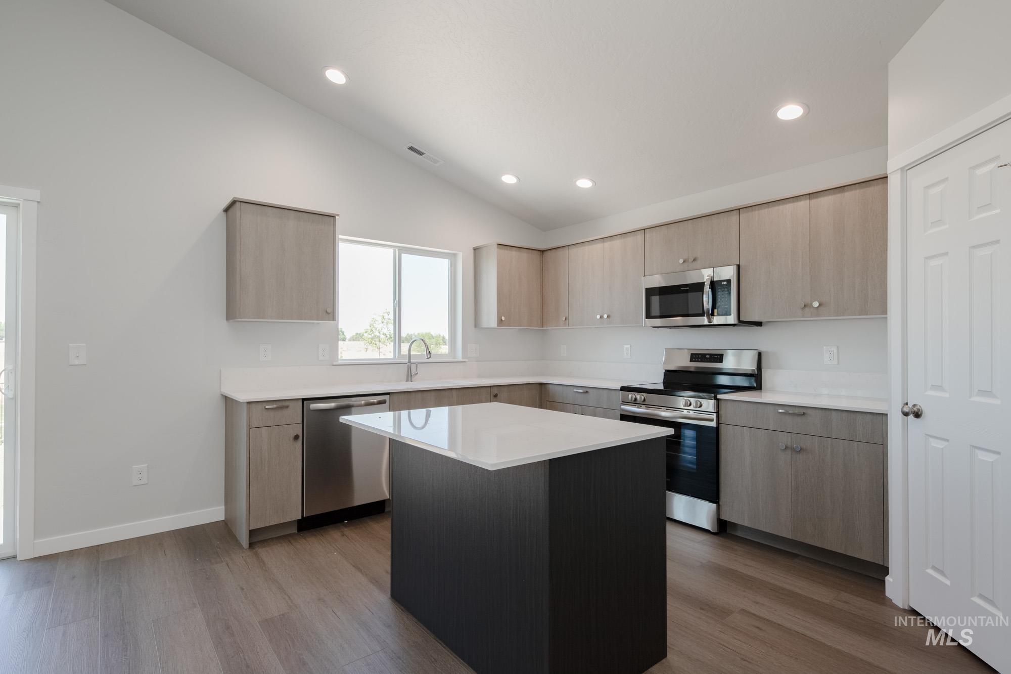 Kitchen featuring vaulted ceiling, appliances with stainless steel finishes, light brown cabinets, wood finished floors, and light countertops