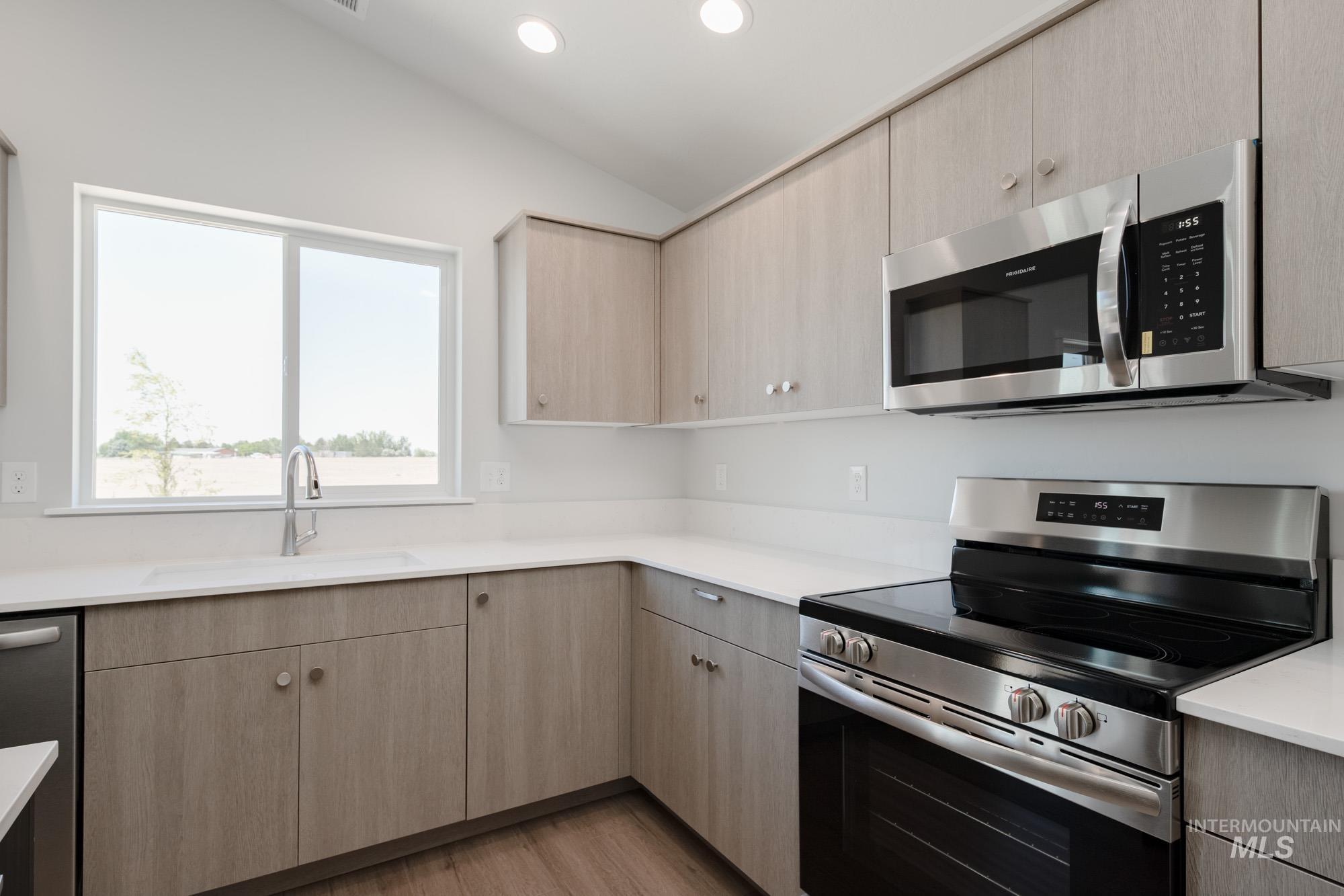 Kitchen featuring stainless steel appliances, lofted ceiling, light brown cabinetry, light countertops, and wood finished floors
