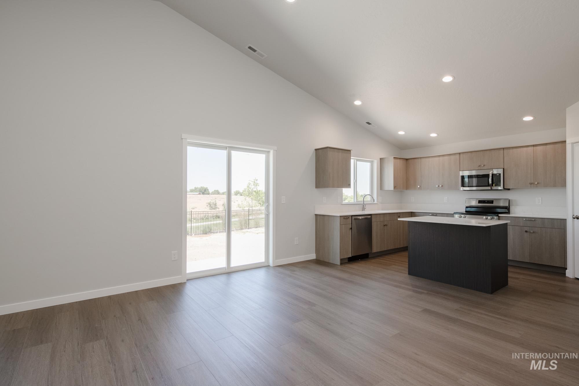 Kitchen with light countertops, wood finished floors, appliances with stainless steel finishes, a kitchen island, and recessed lighting