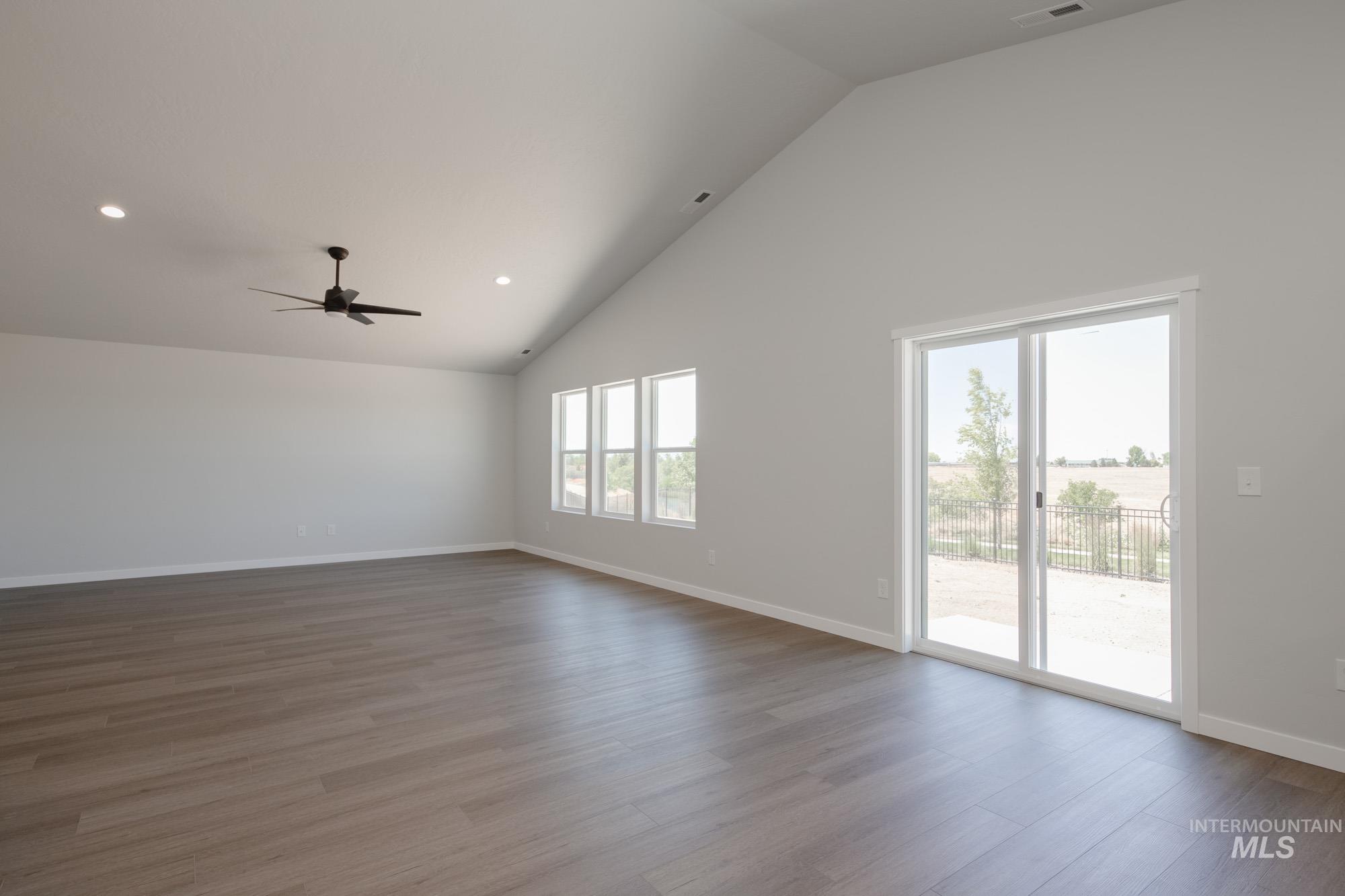 Empty room with wood finished floors, high vaulted ceiling, ceiling fan, and recessed lighting