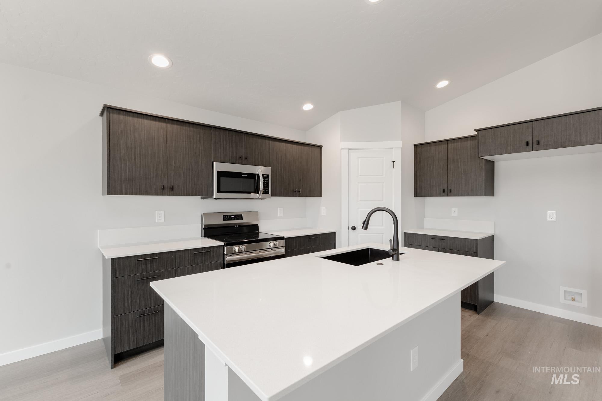 Kitchen featuring vaulted ceiling, appliances with stainless steel finishes, light countertops, dark brown cabinets, and light wood-type flooring