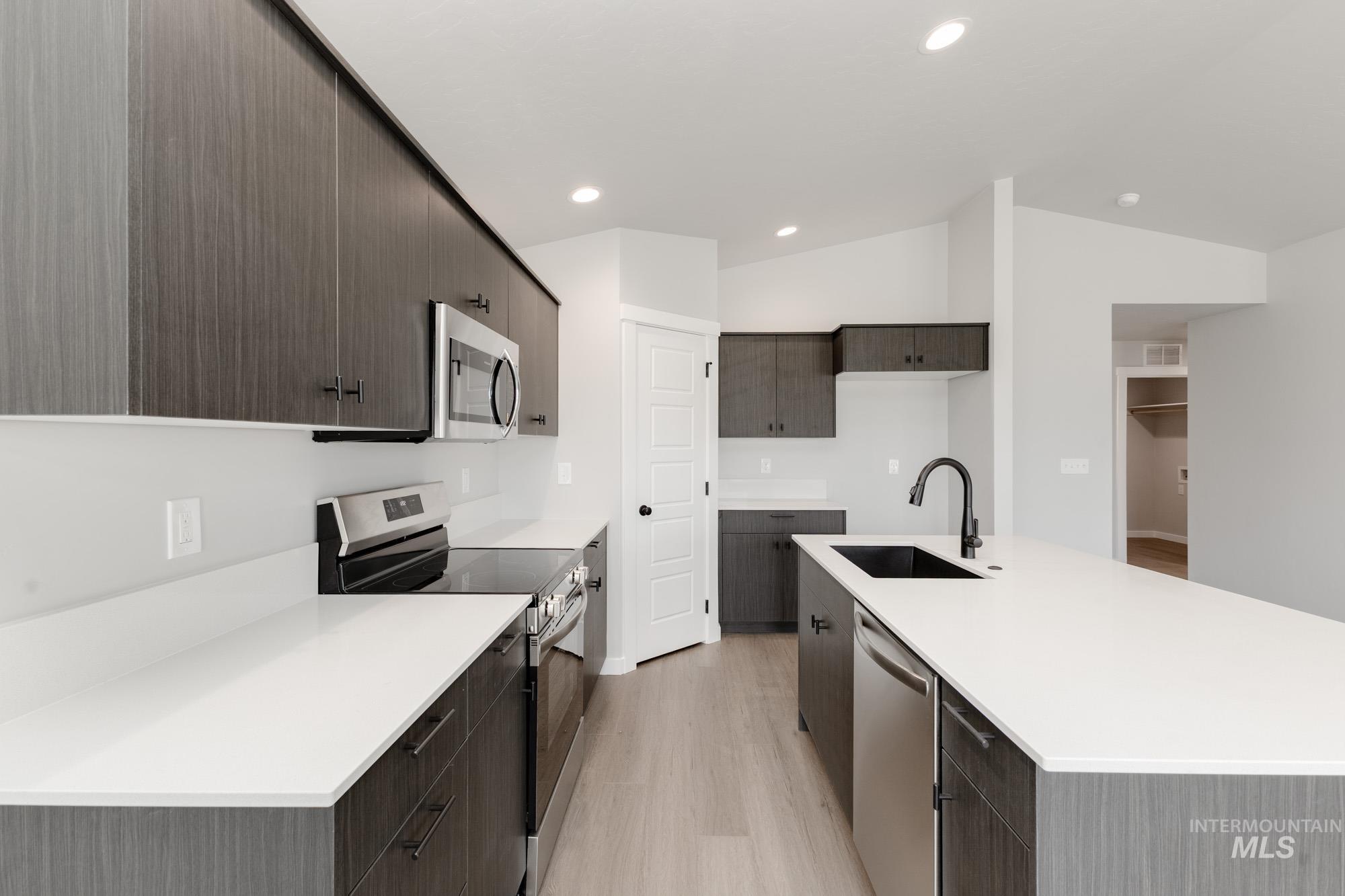 Kitchen featuring vaulted ceiling, appliances with stainless steel finishes, light wood-type flooring, dark brown cabinets, and a center island with sink