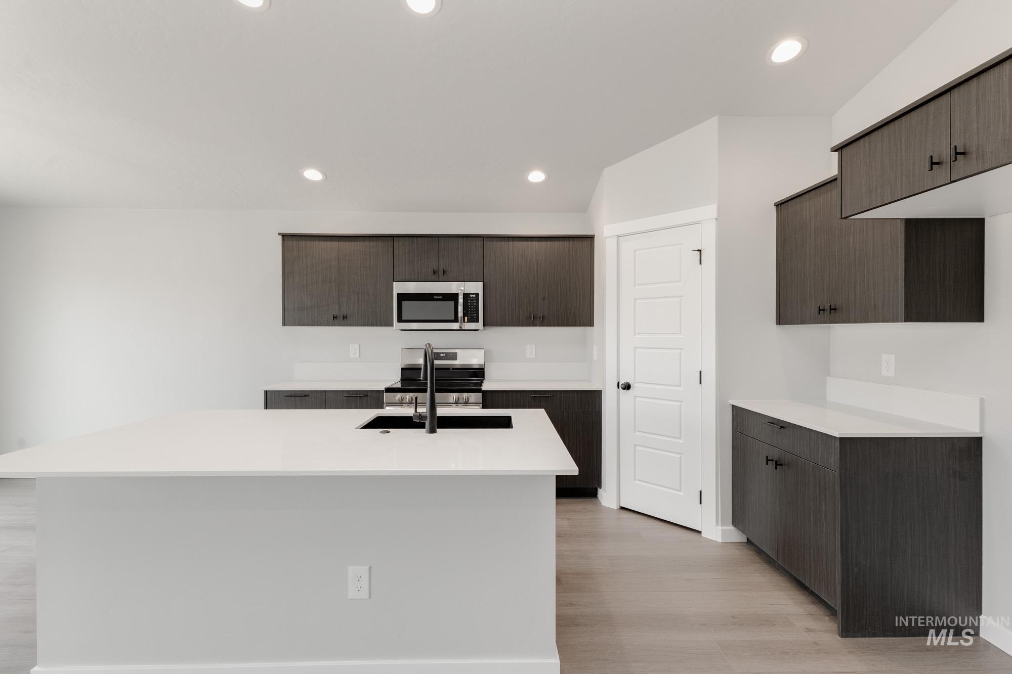 Kitchen featuring recessed lighting, light wood-style floors, stainless steel appliances, light countertops, and dark brown cabinets
