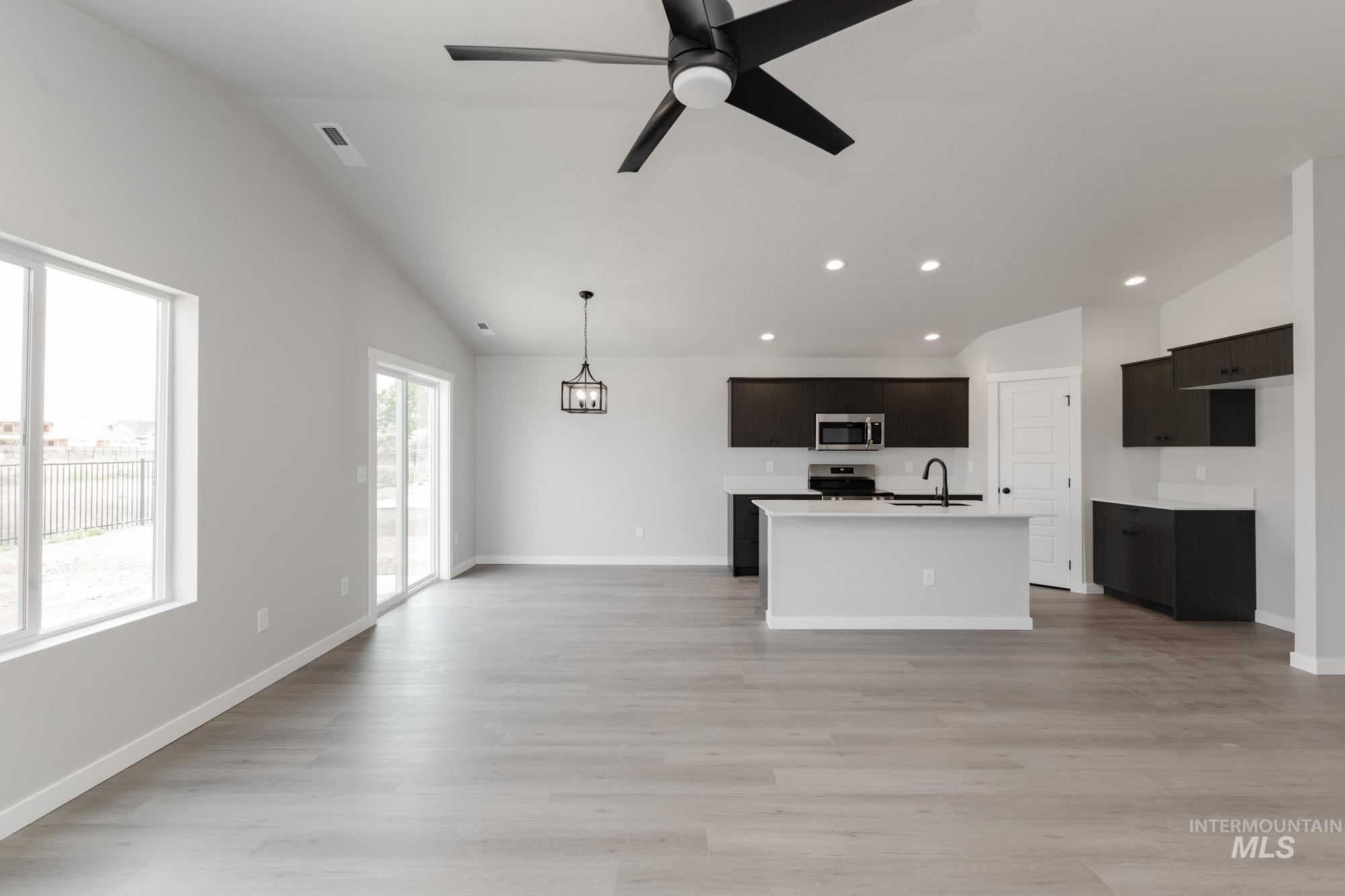 Kitchen with open floor plan, a center island with sink, light wood-type flooring, stainless steel microwave, and recessed lighting
