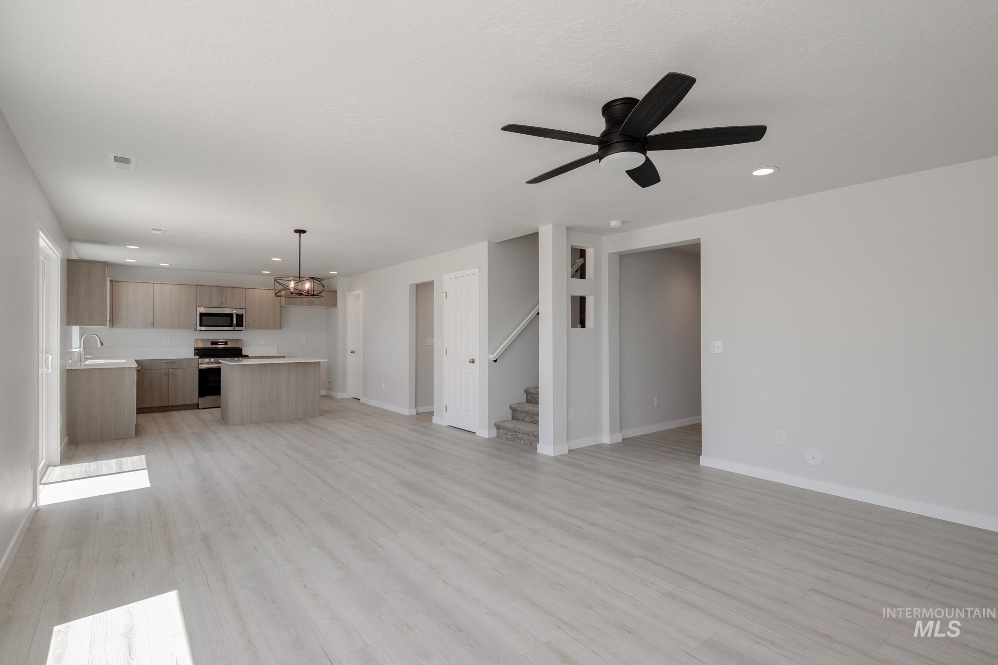 Unfurnished living room with a chandelier, recessed lighting, light wood-style floors, stairs, and a ceiling fan