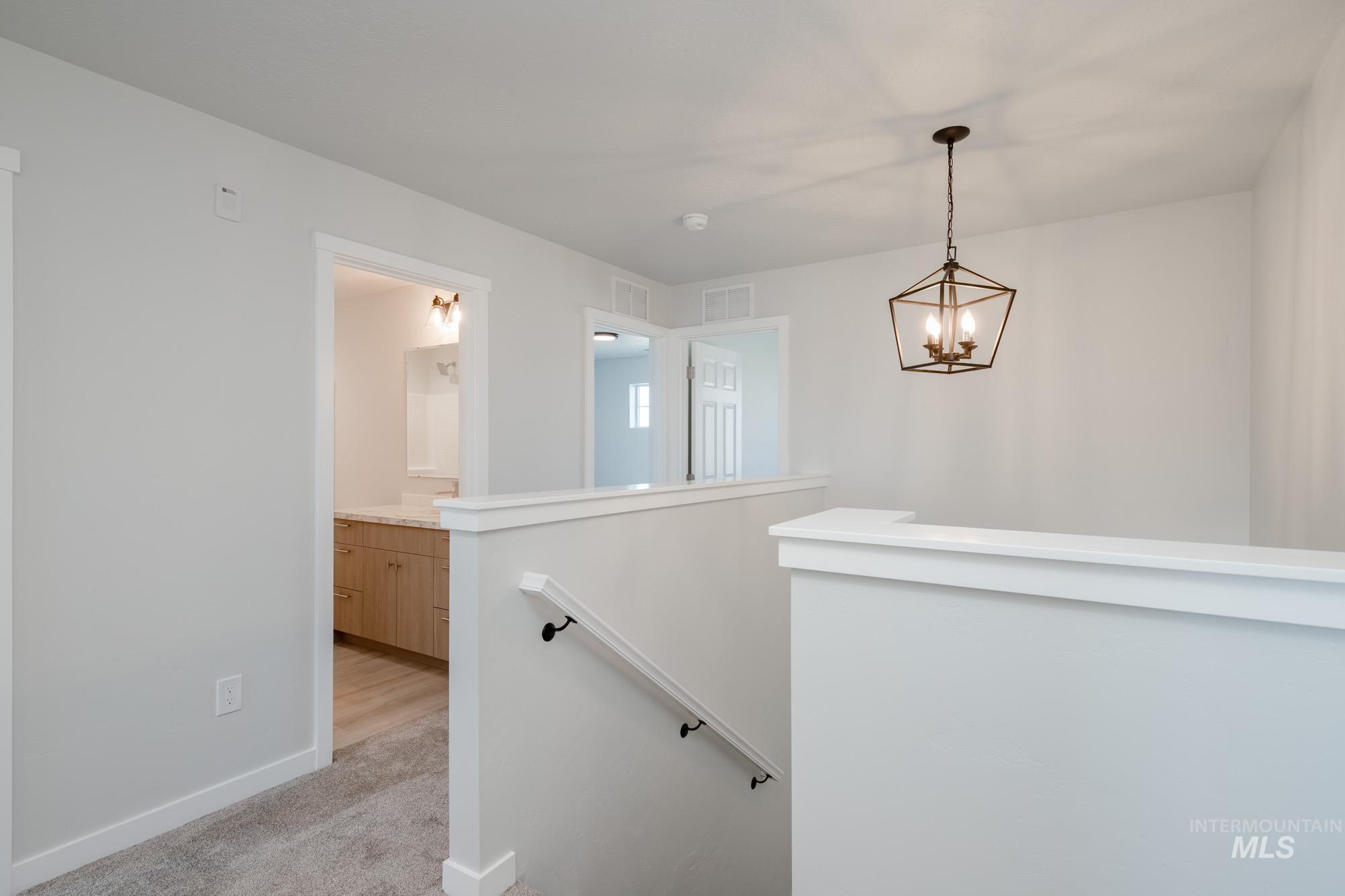 Hall with an upstairs landing, light carpet, and a chandelier