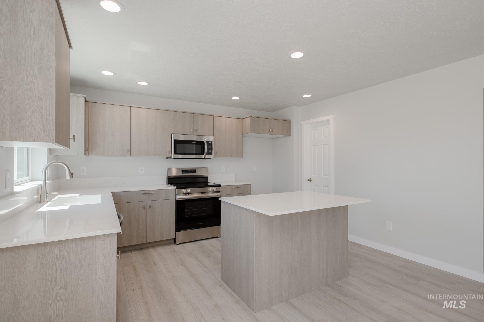 Kitchen featuring light brown cabinets, stainless steel appliances, light countertops, light wood-type flooring, and recessed lighting