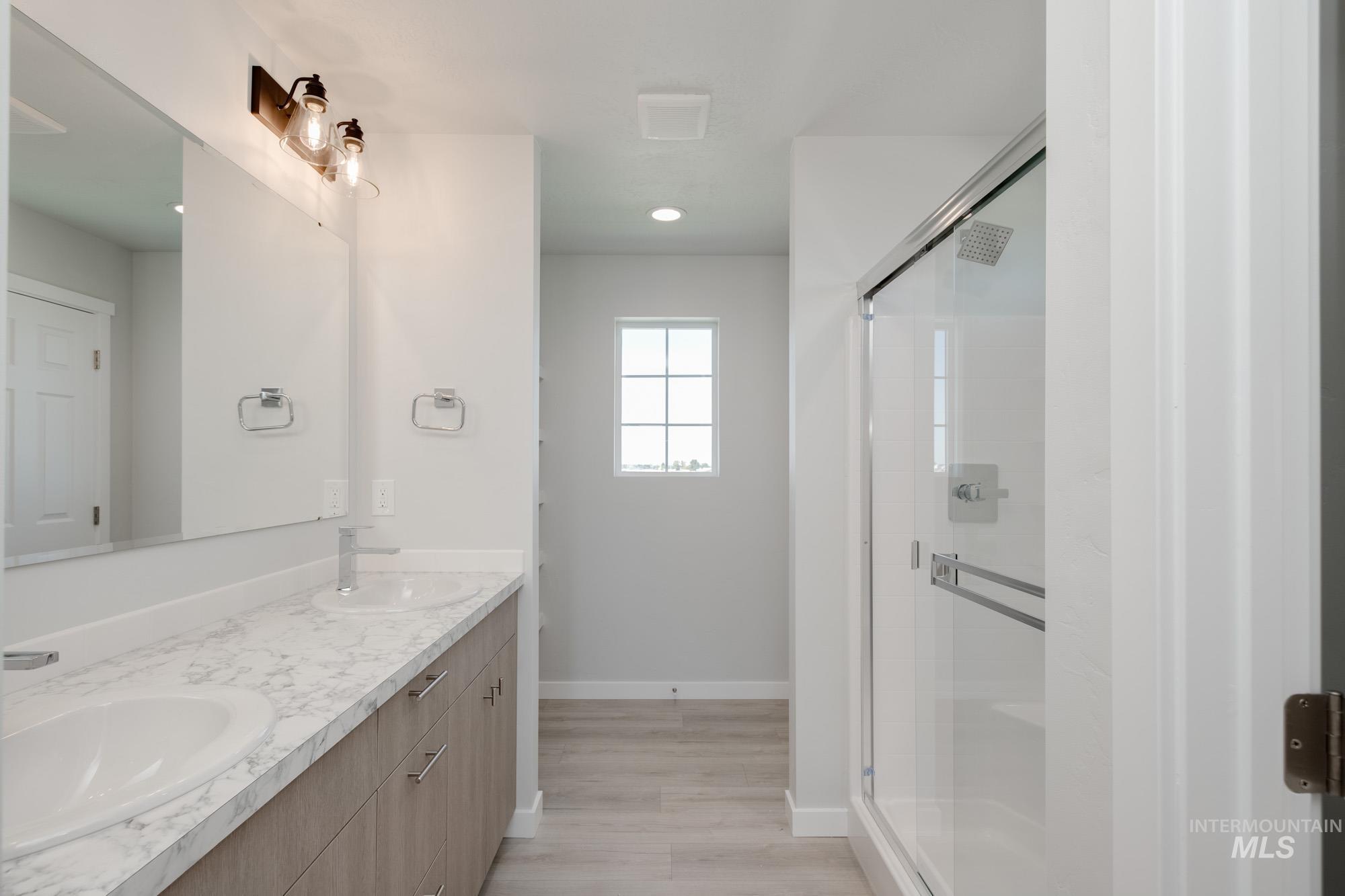 Bathroom featuring double vanity, a shower stall, recessed lighting, and wood finished floors