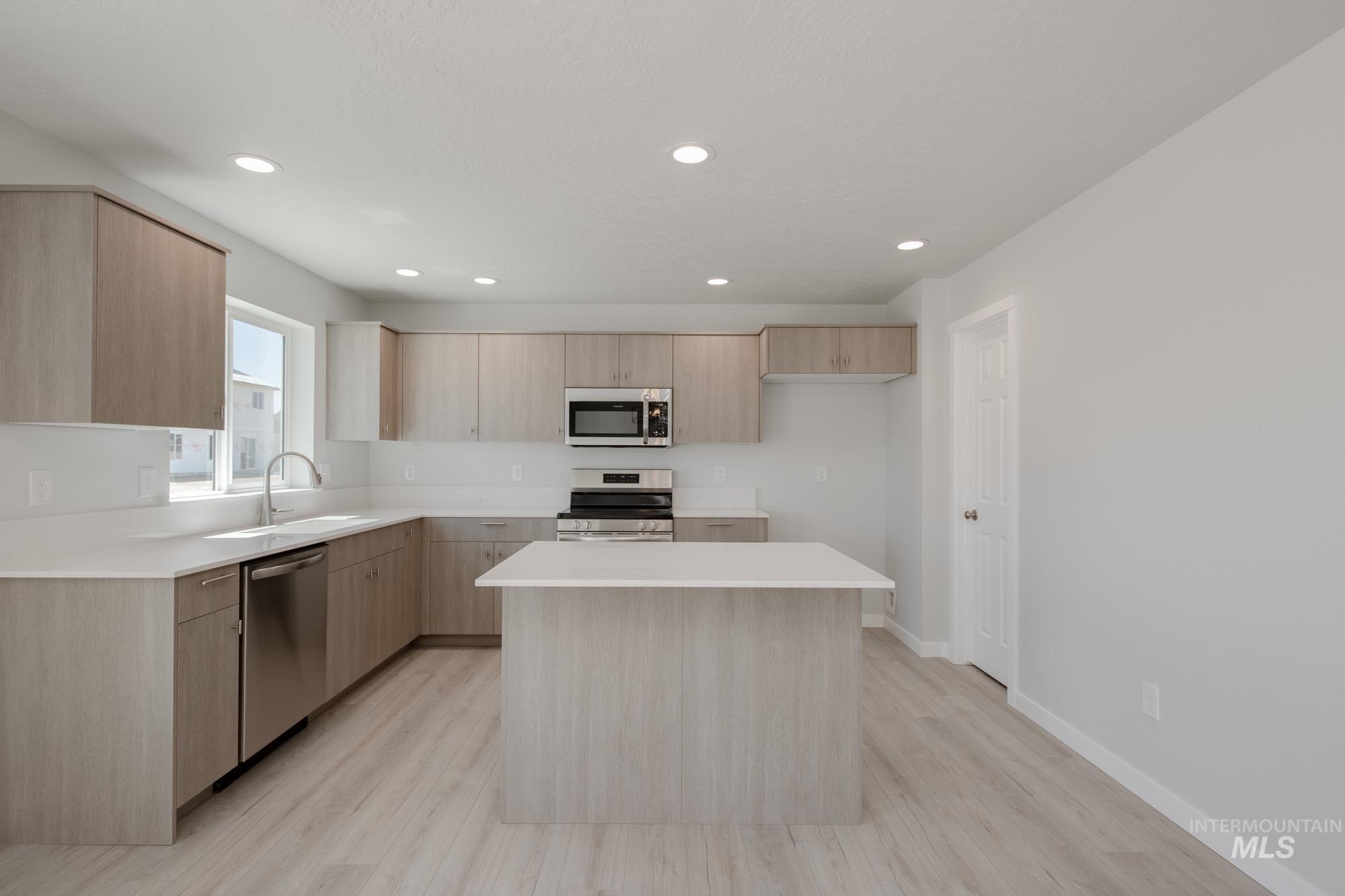 Kitchen featuring light brown cabinets, a kitchen island, appliances with stainless steel finishes, light countertops, and recessed lighting