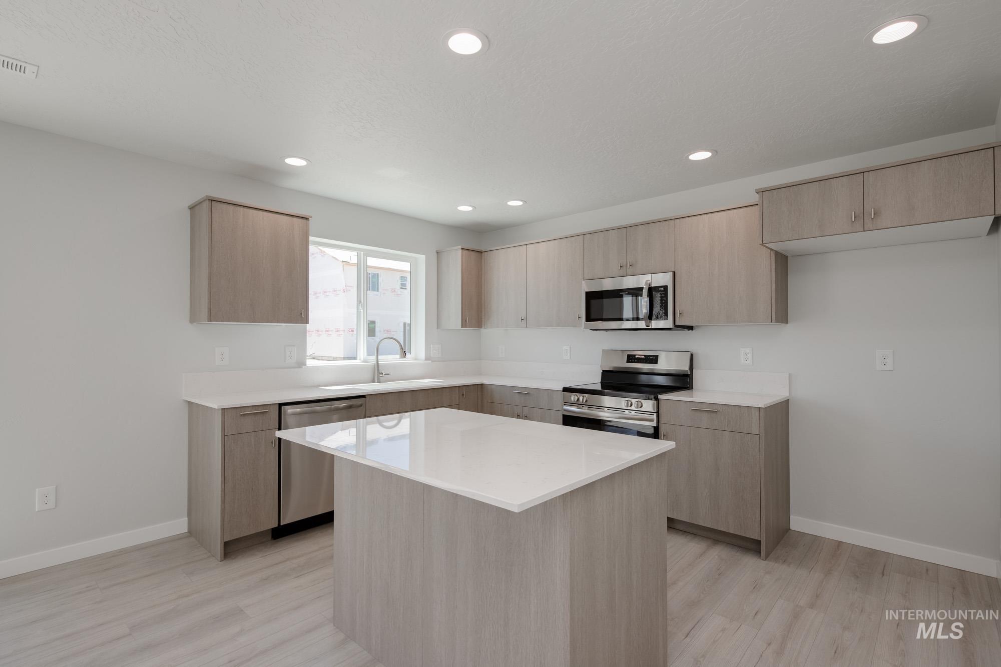 Kitchen featuring light brown cabinetry, appliances with stainless steel finishes, light countertops, recessed lighting, and a kitchen island