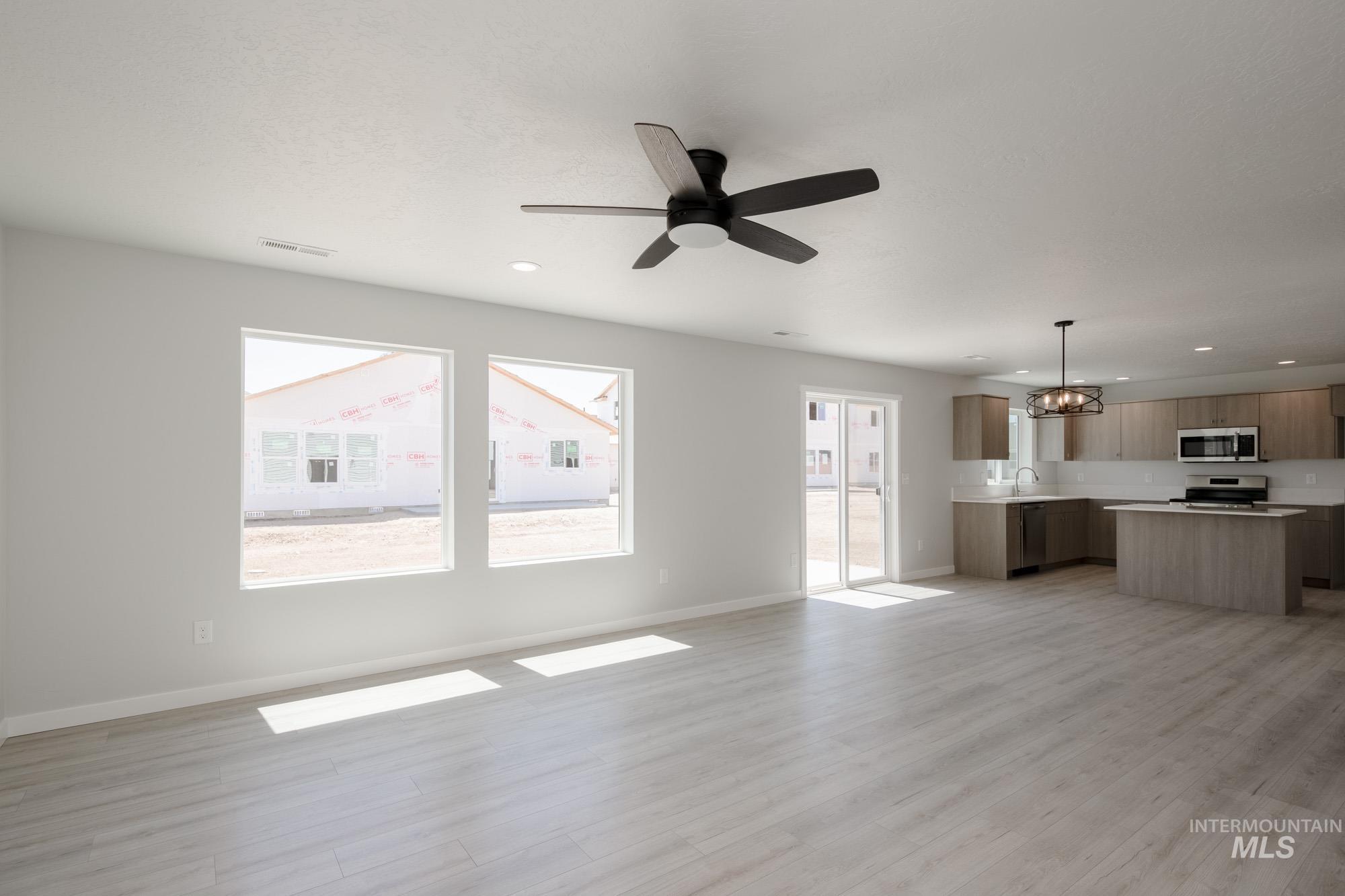 Unfurnished living room featuring healthy amount of natural light, light wood-style flooring, a chandelier, a ceiling fan, and recessed lighting