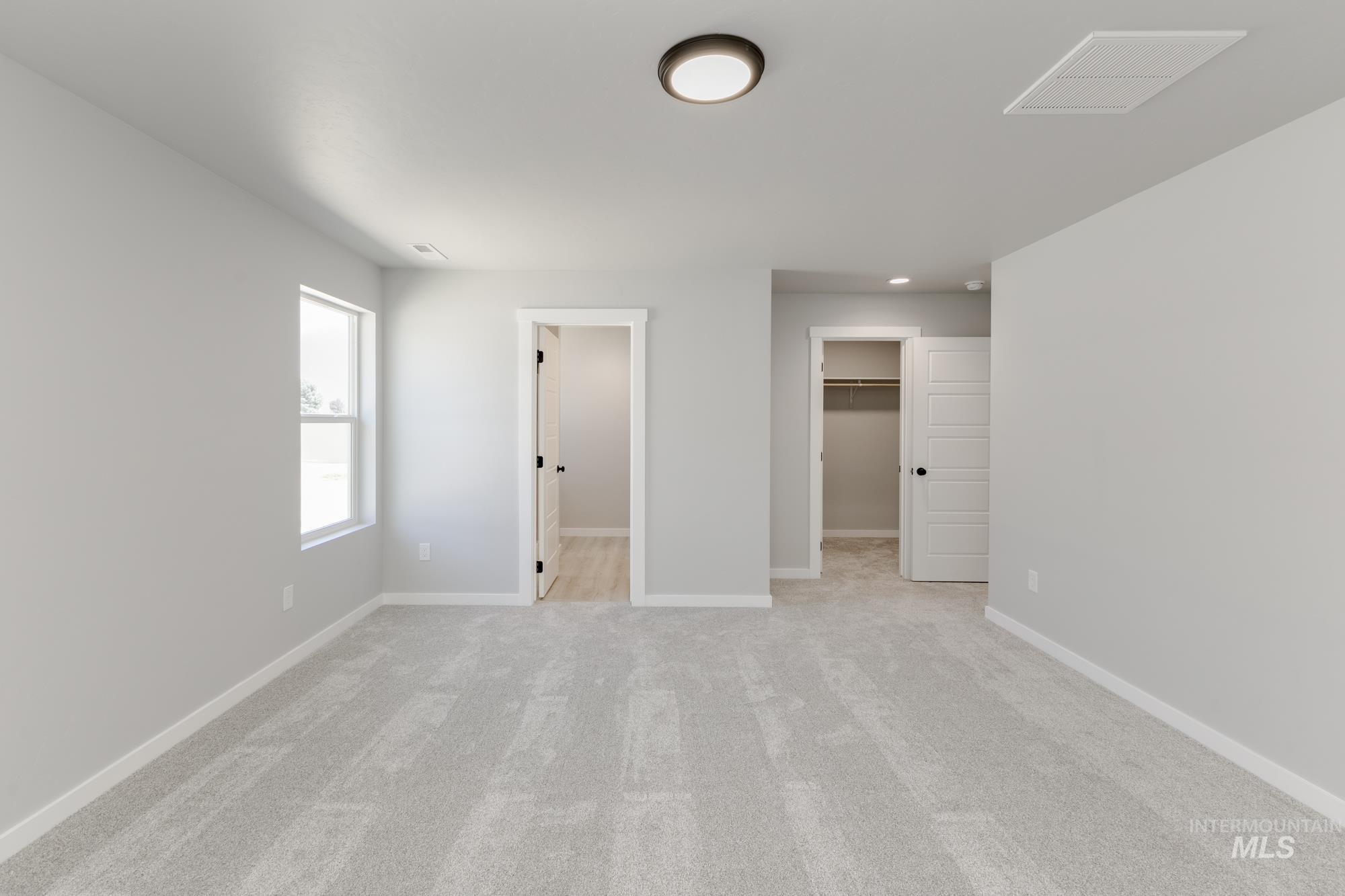 Unfurnished bedroom featuring light colored carpet and a walk in closet