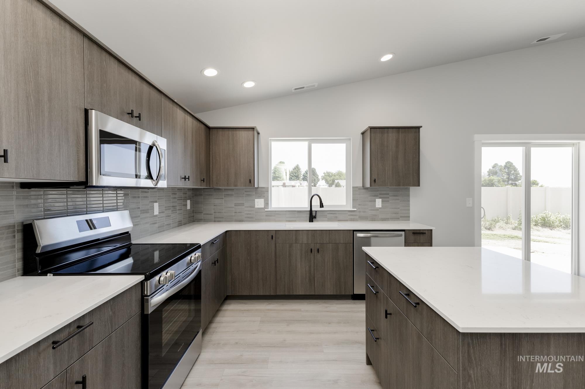 Kitchen featuring appliances with stainless steel finishes, lofted ceiling, tasteful backsplash, recessed lighting, and light wood-type flooring