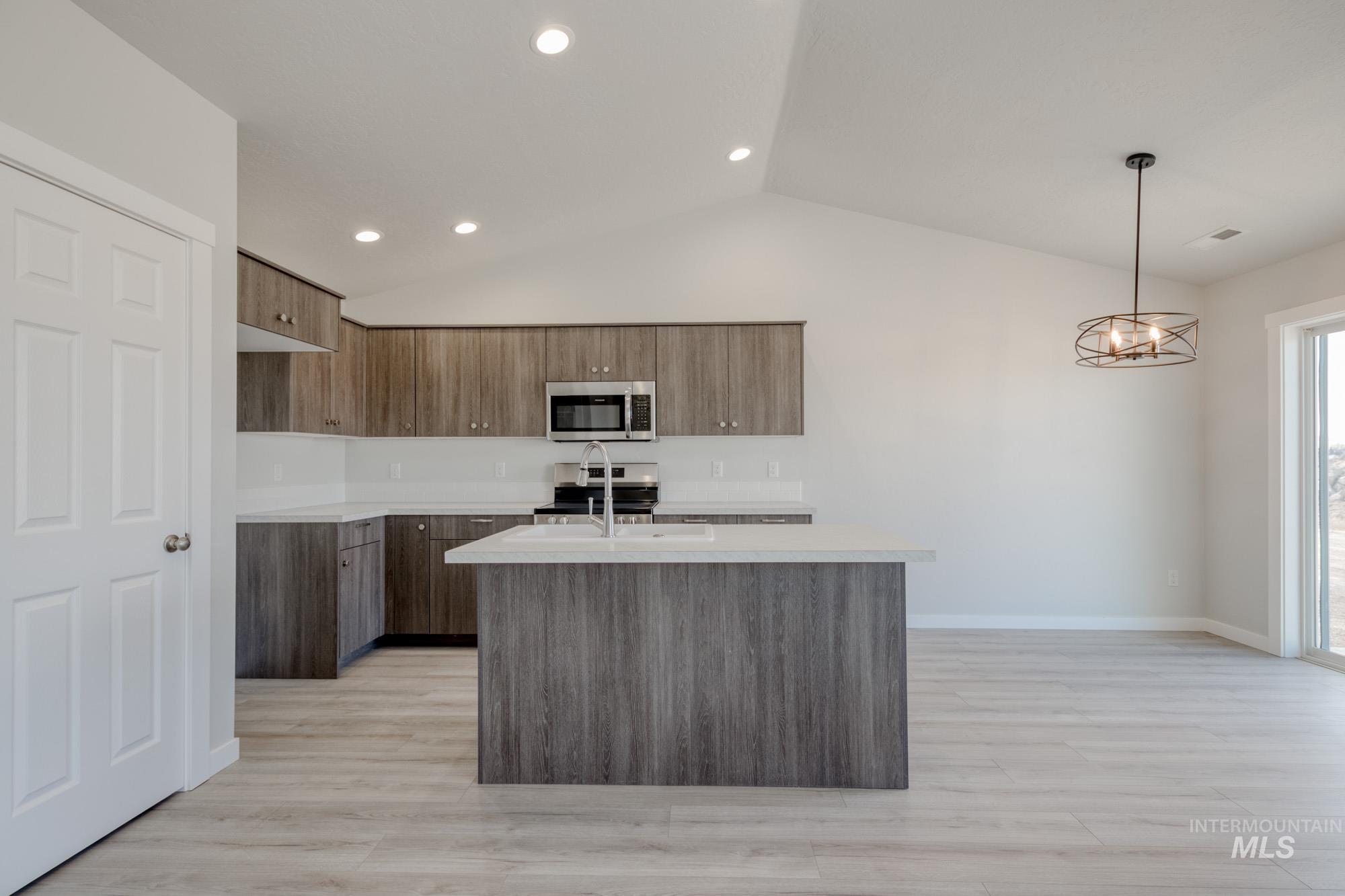 Kitchen with lofted ceiling, decorative light fixtures, modern cabinets, appliances with stainless steel finishes, and an island with sink