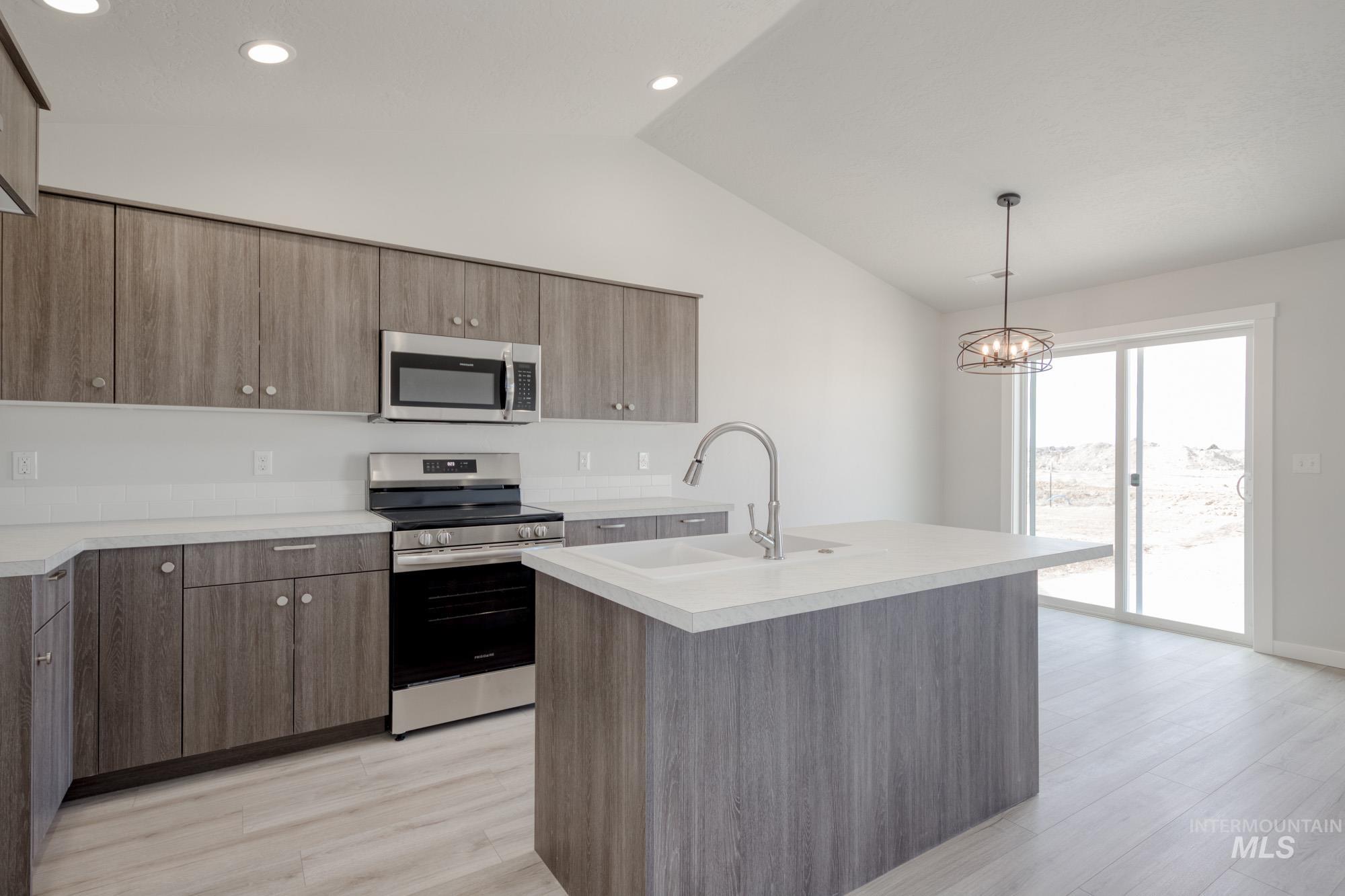 Kitchen featuring appliances with stainless steel finishes, light countertops, hanging light fixtures, lofted ceiling, and light wood-style floors