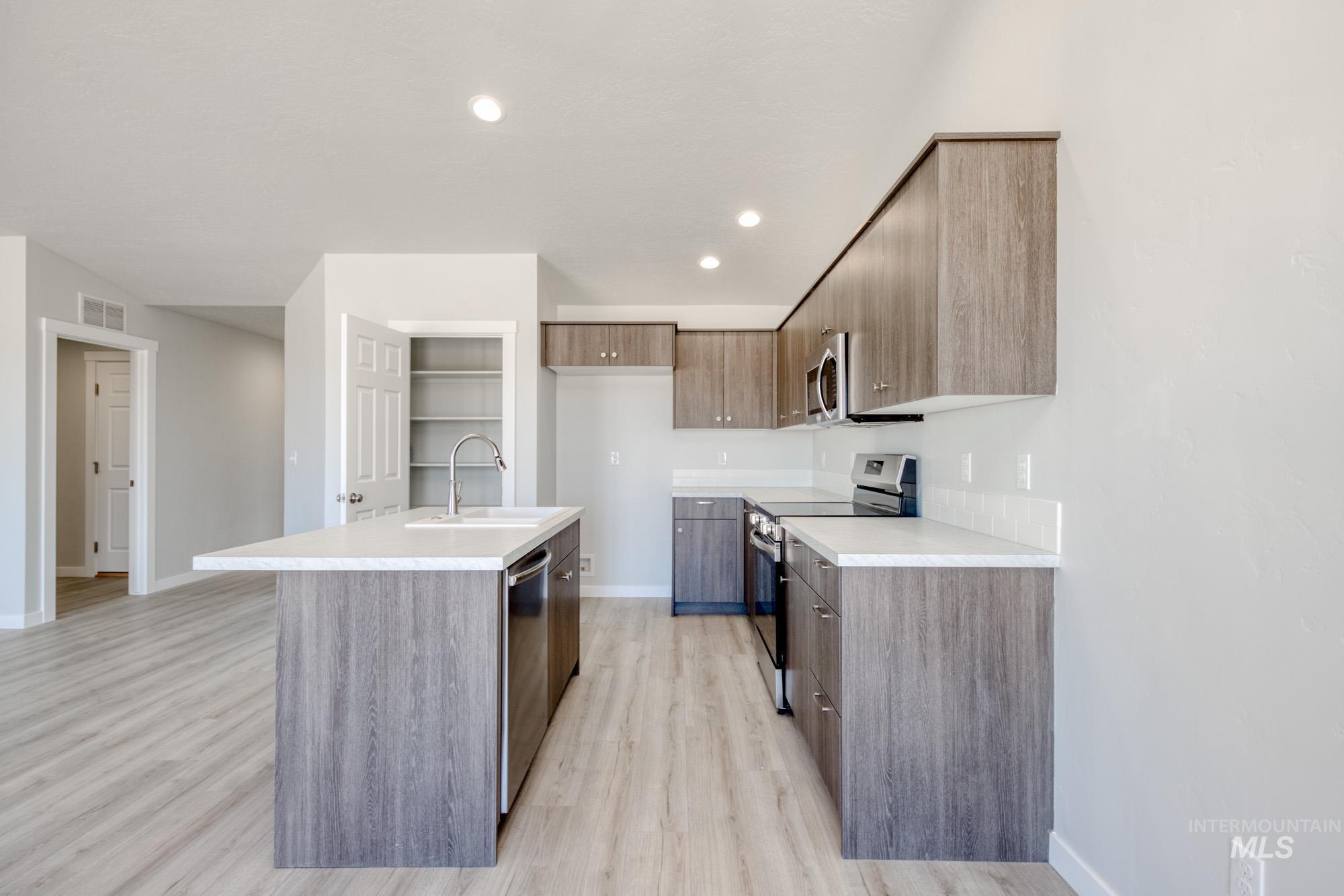 Kitchen with modern cabinets, stainless steel appliances, light countertops, an island with sink, and recessed lighting