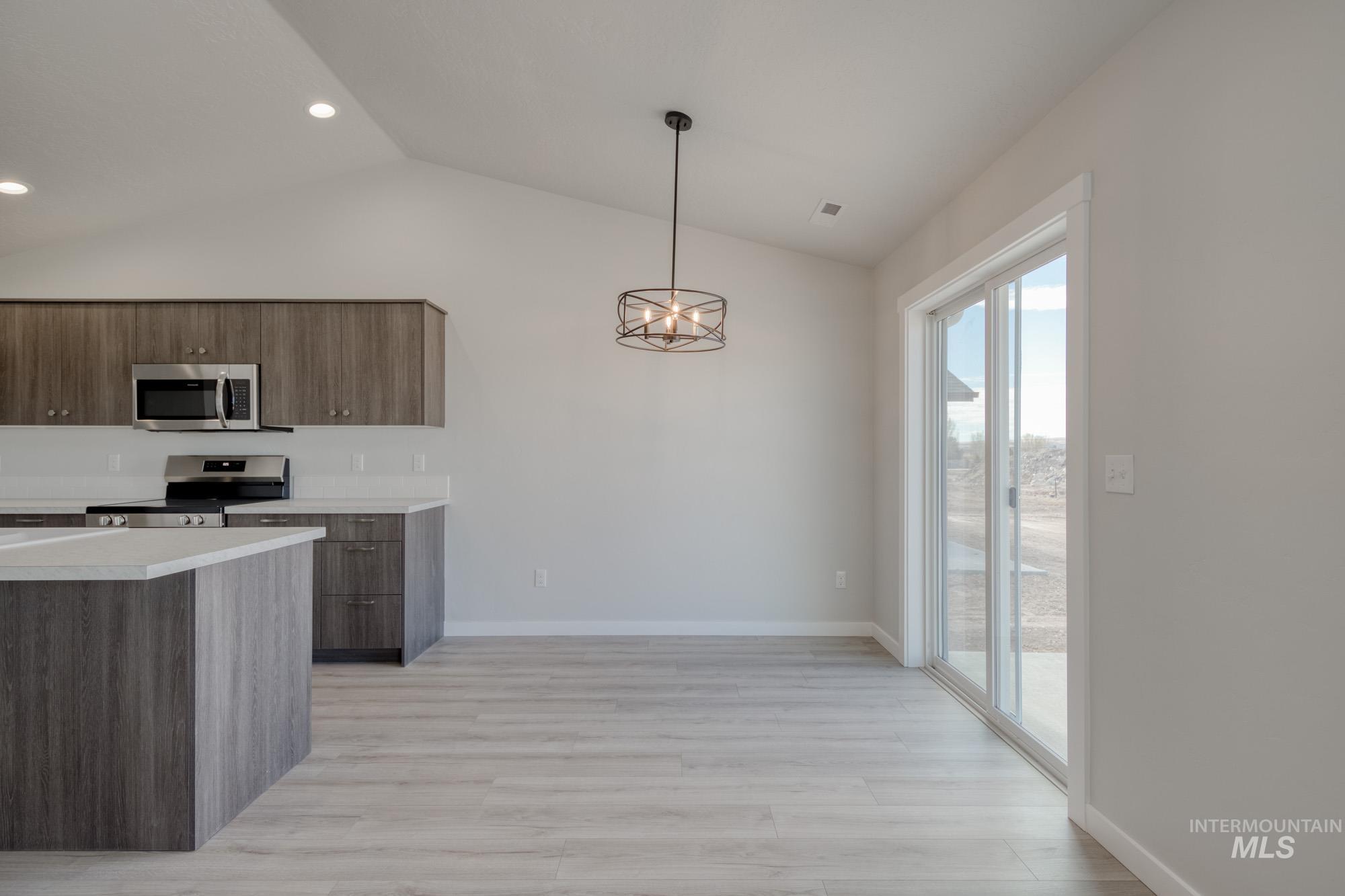 Kitchen featuring light countertops, appliances with stainless steel finishes, vaulted ceiling, light wood-type flooring, and pendant lighting