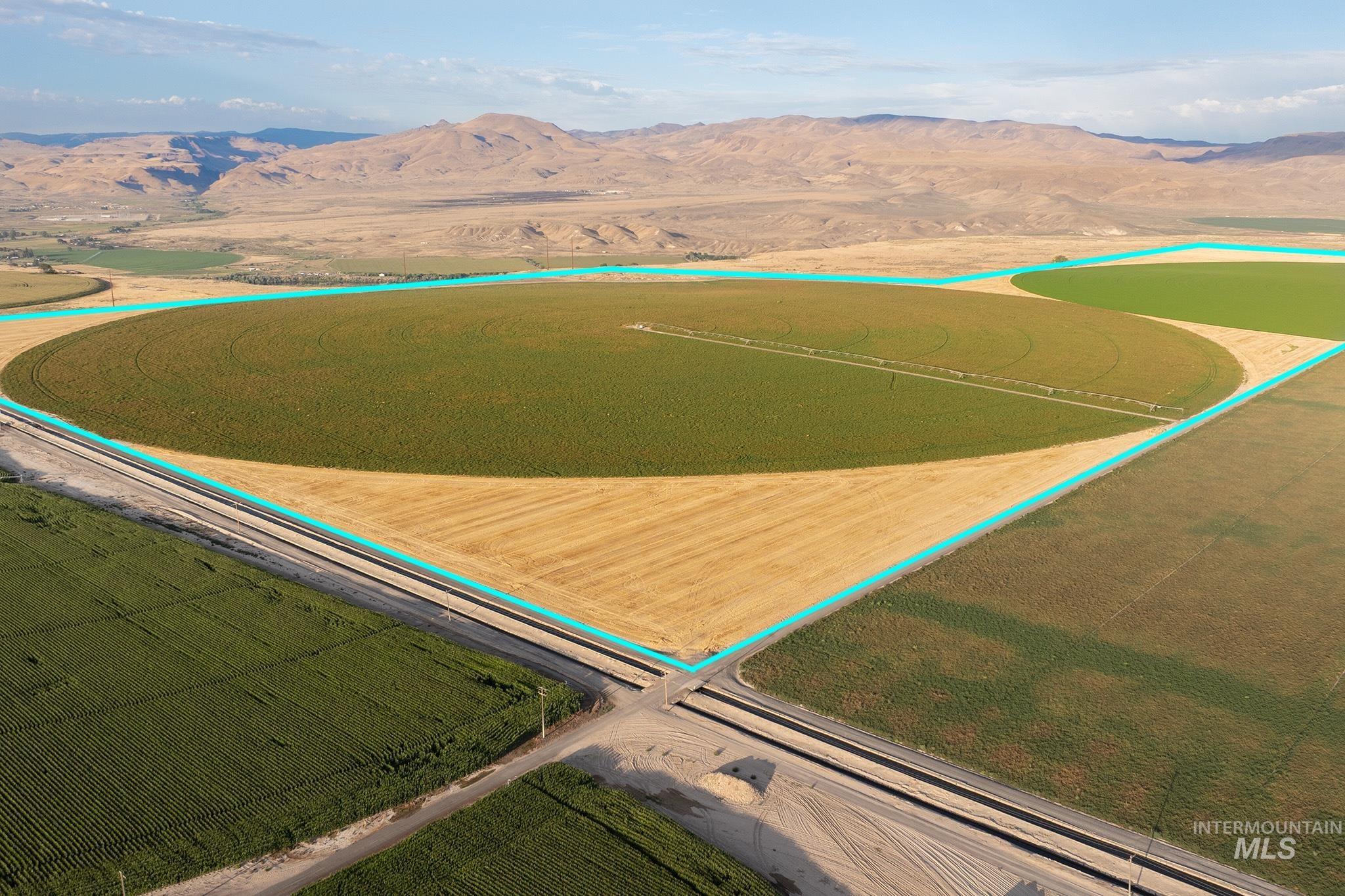 Overview of rural landscape featuring property parcel outlined, a mountain backdrop, and rows of crops