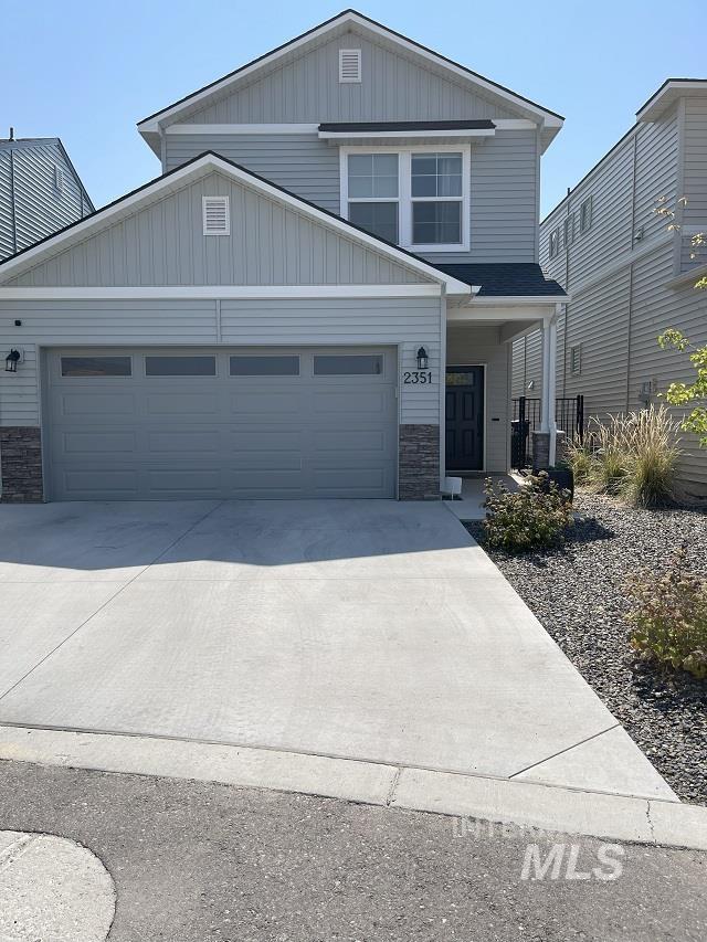 View of front facade featuring stone siding, an attached garage, driveway, and board and batten siding
