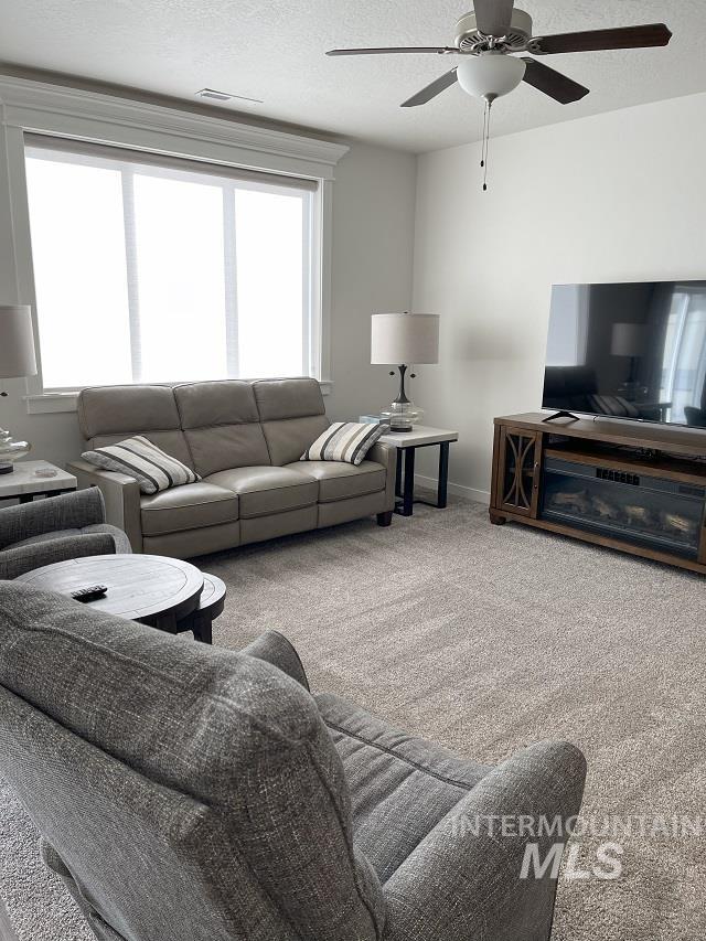 Carpeted living area with a textured ceiling and ceiling fan
