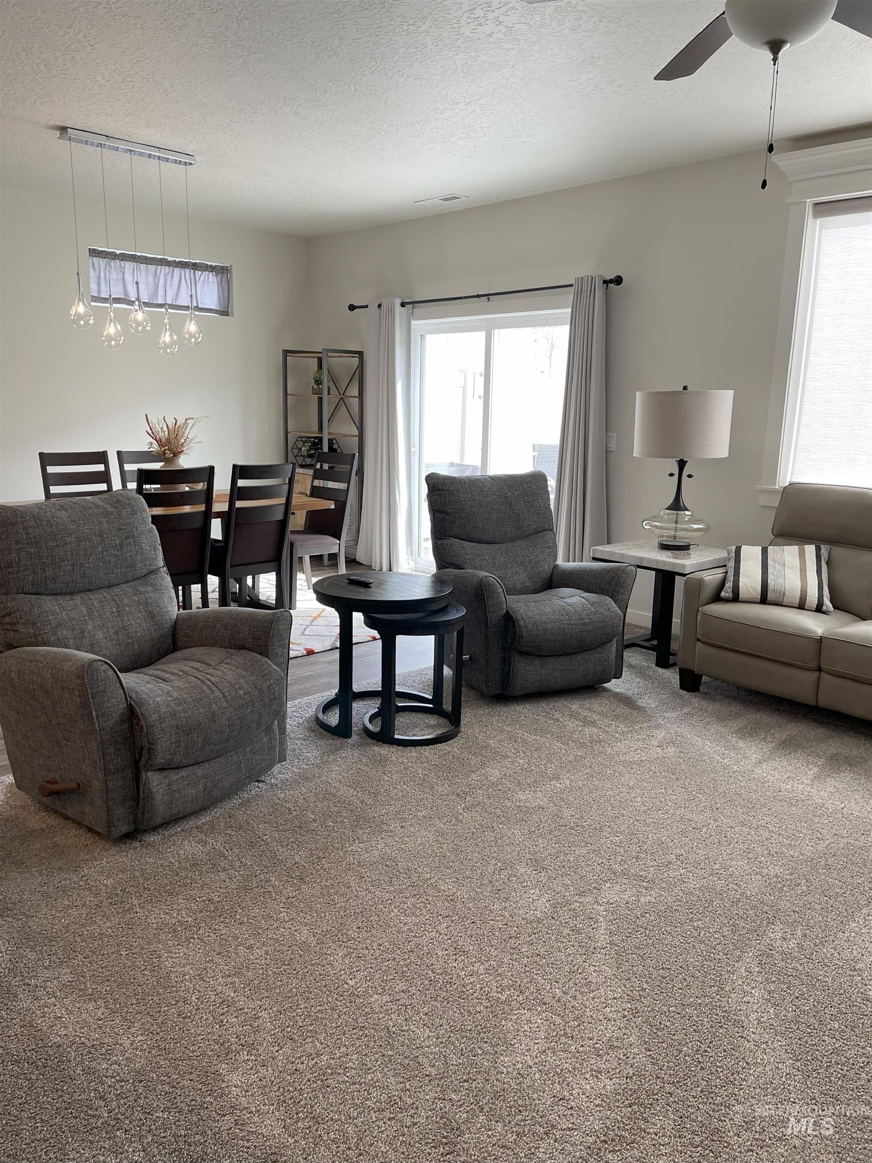Living area with a textured ceiling, light carpet, and a ceiling fan