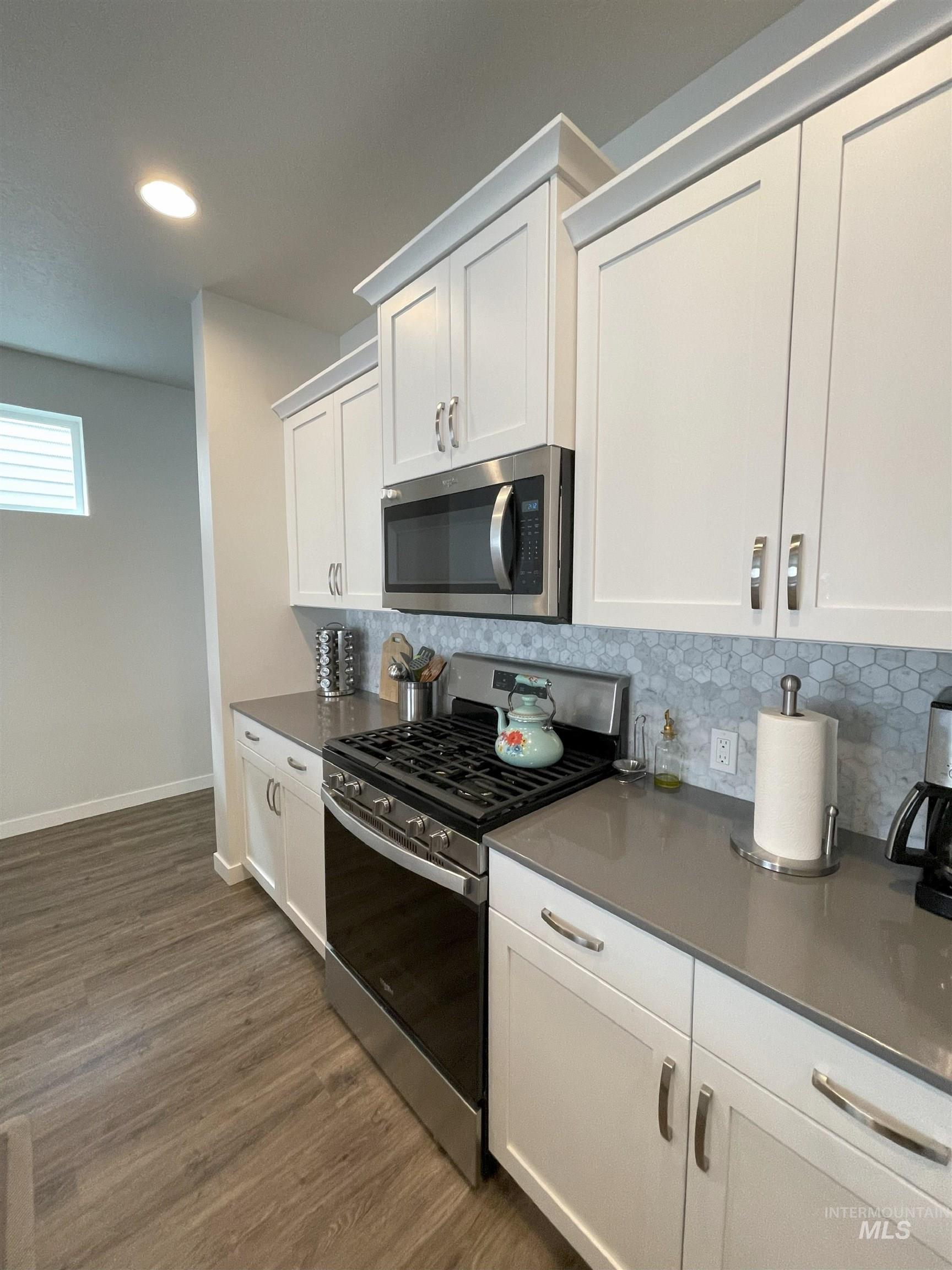 Kitchen with appliances with stainless steel finishes, decorative backsplash, white cabinets, dark wood-type flooring, and recessed lighting