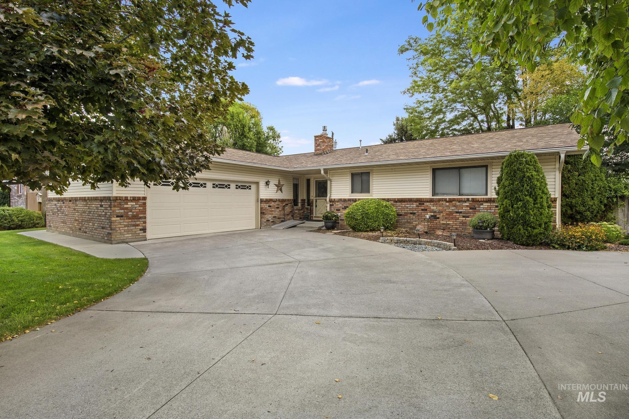 Ranch-style home with an attached garage, driveway, a chimney, and brick siding