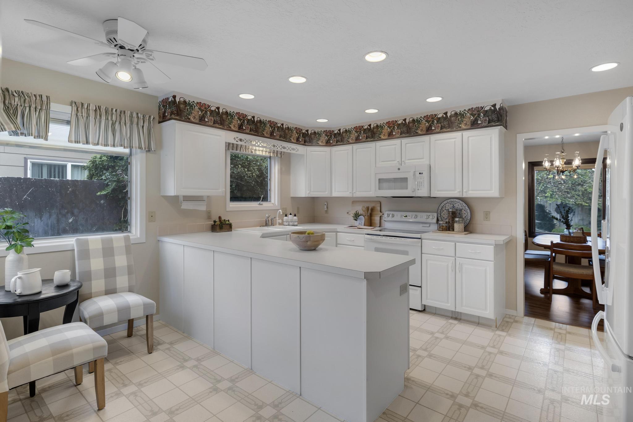 Kitchen featuring white appliances, light countertops, recessed lighting, white cabinets, and a chandelier