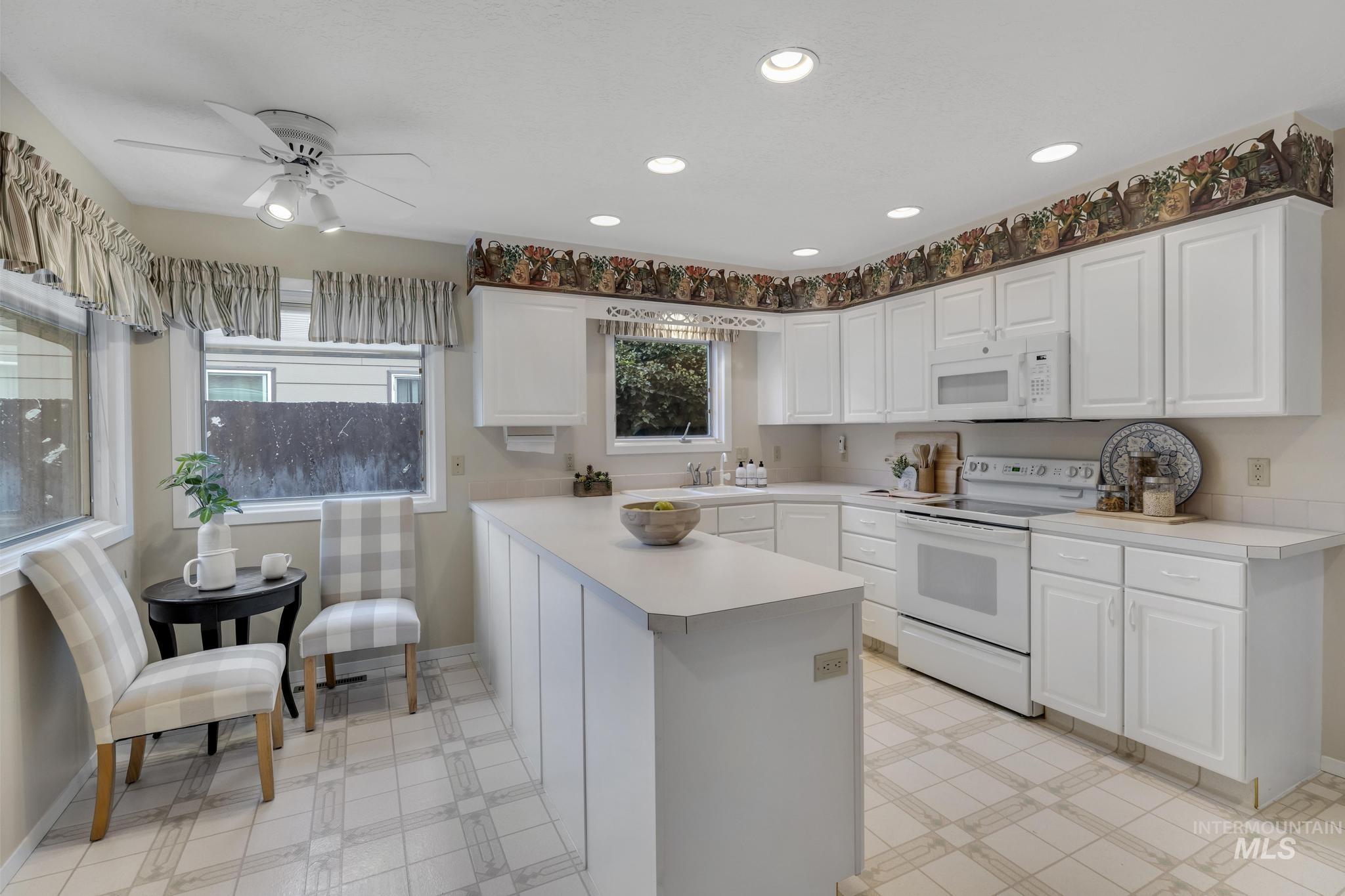 Kitchen with light countertops, white appliances, recessed lighting, healthy amount of natural light, and white cabinets
