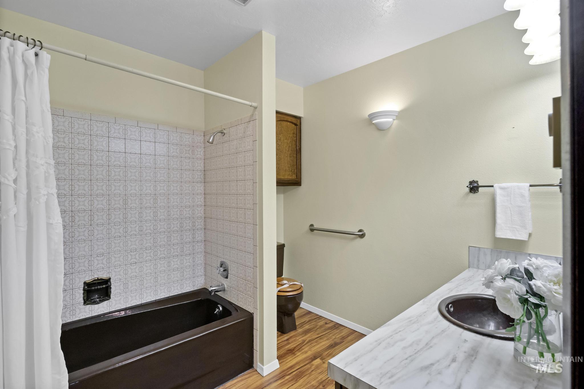 Full bath with shower / bath combo, vanity, and light wood-type flooring
