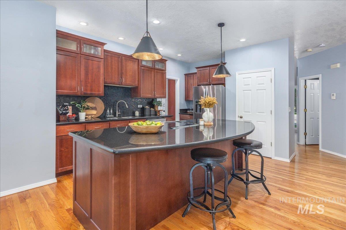 Kitchen featuring stainless steel fridge, dark countertops, light wood finished floors, tasteful backsplash, and an island with sink