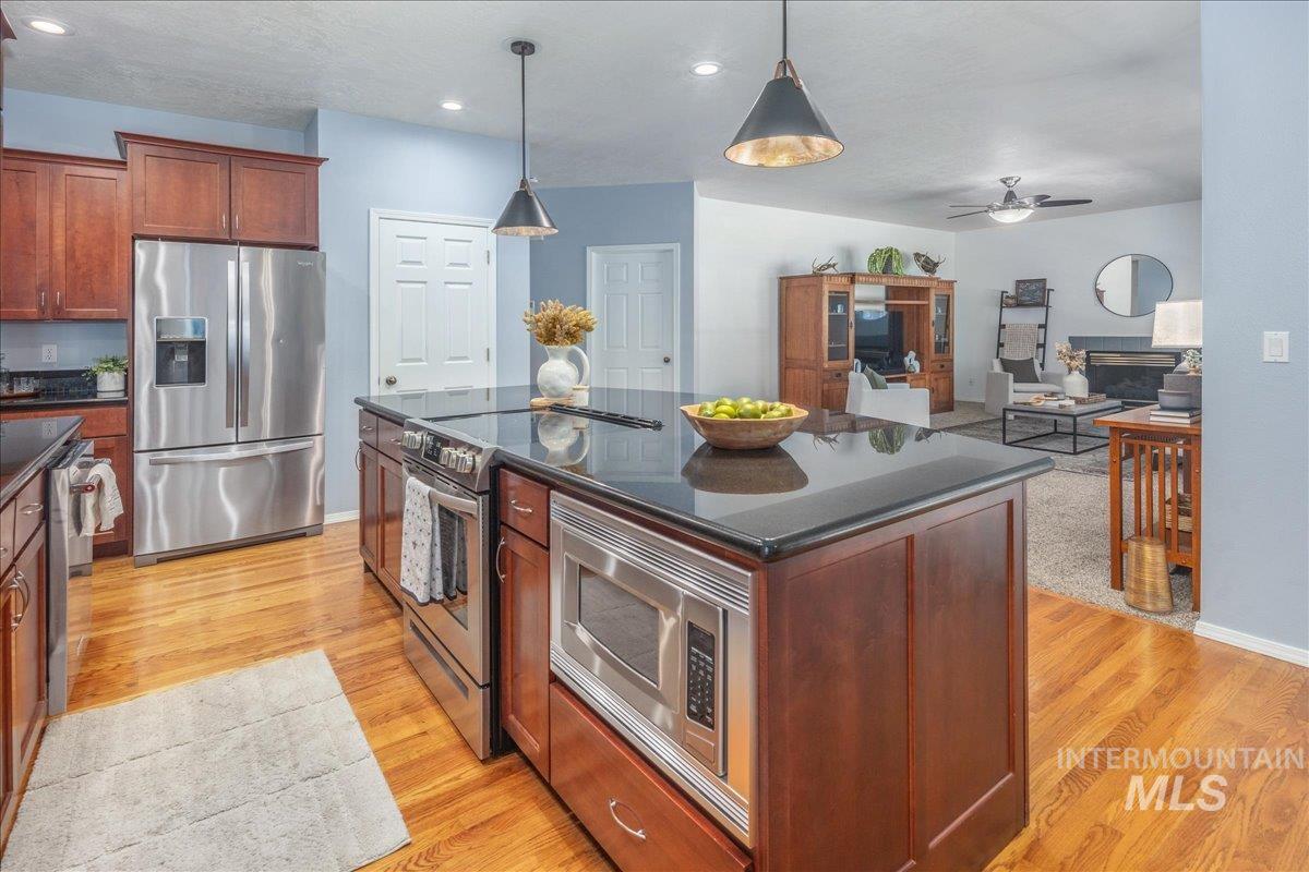 Kitchen featuring appliances with stainless steel finishes, dark countertops, ceiling fan, light wood finished floors, and pendant lighting